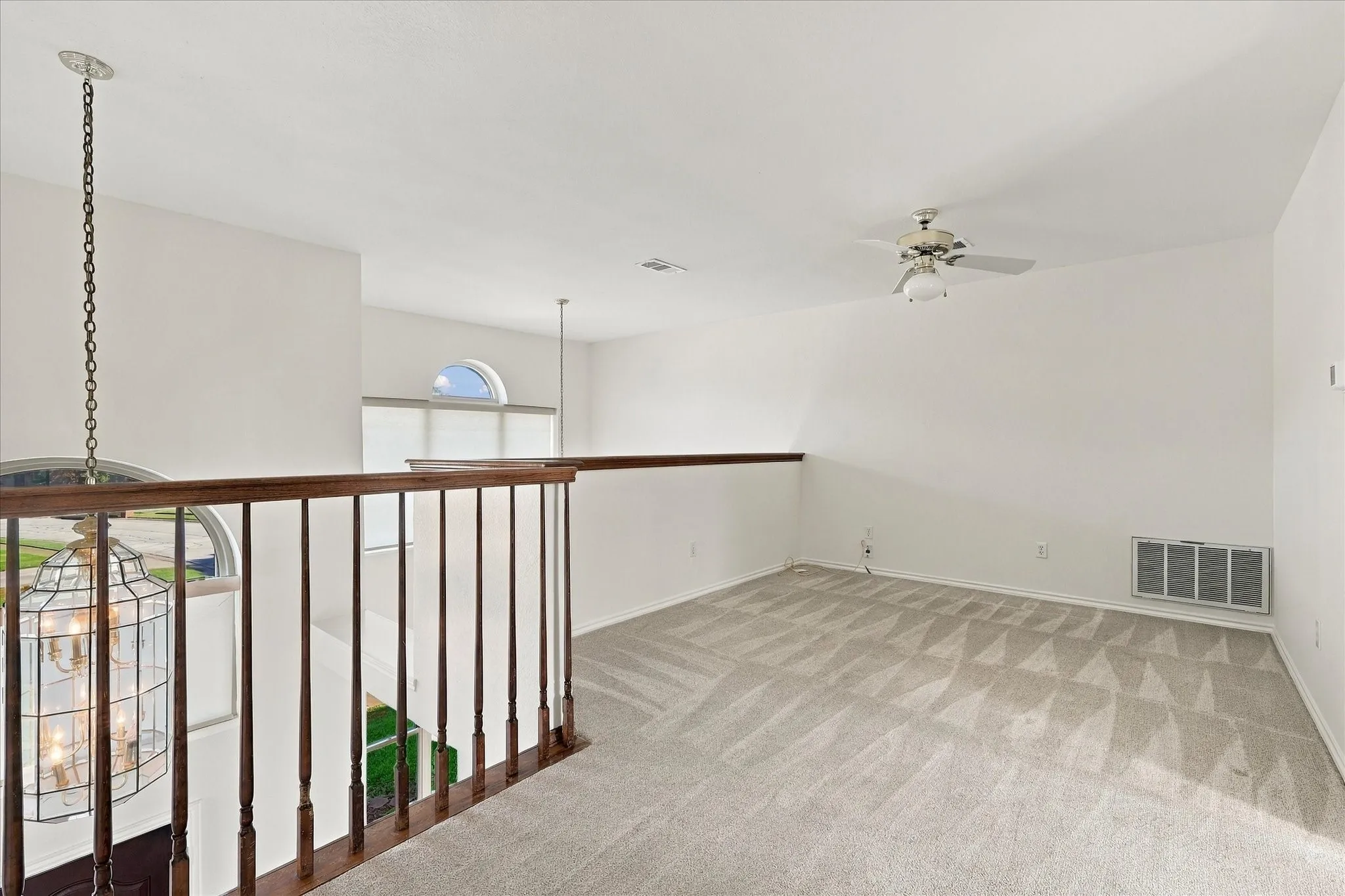 Carpeted loft area with a ceiling fan, arched window, and wood spindle railing
