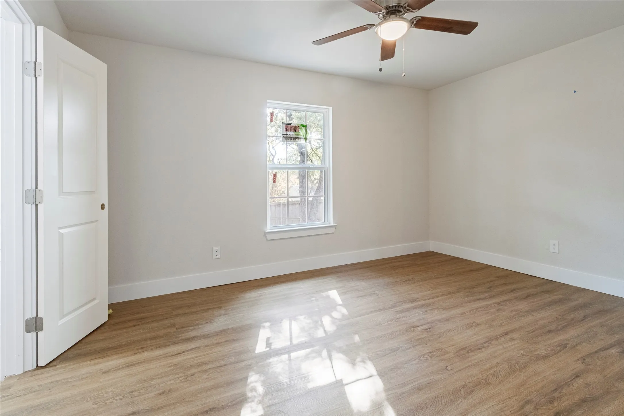 Neutral wall tones, wood-finish flooring, white trim, a double-panel door, and a ceiling fan with integrated lighting