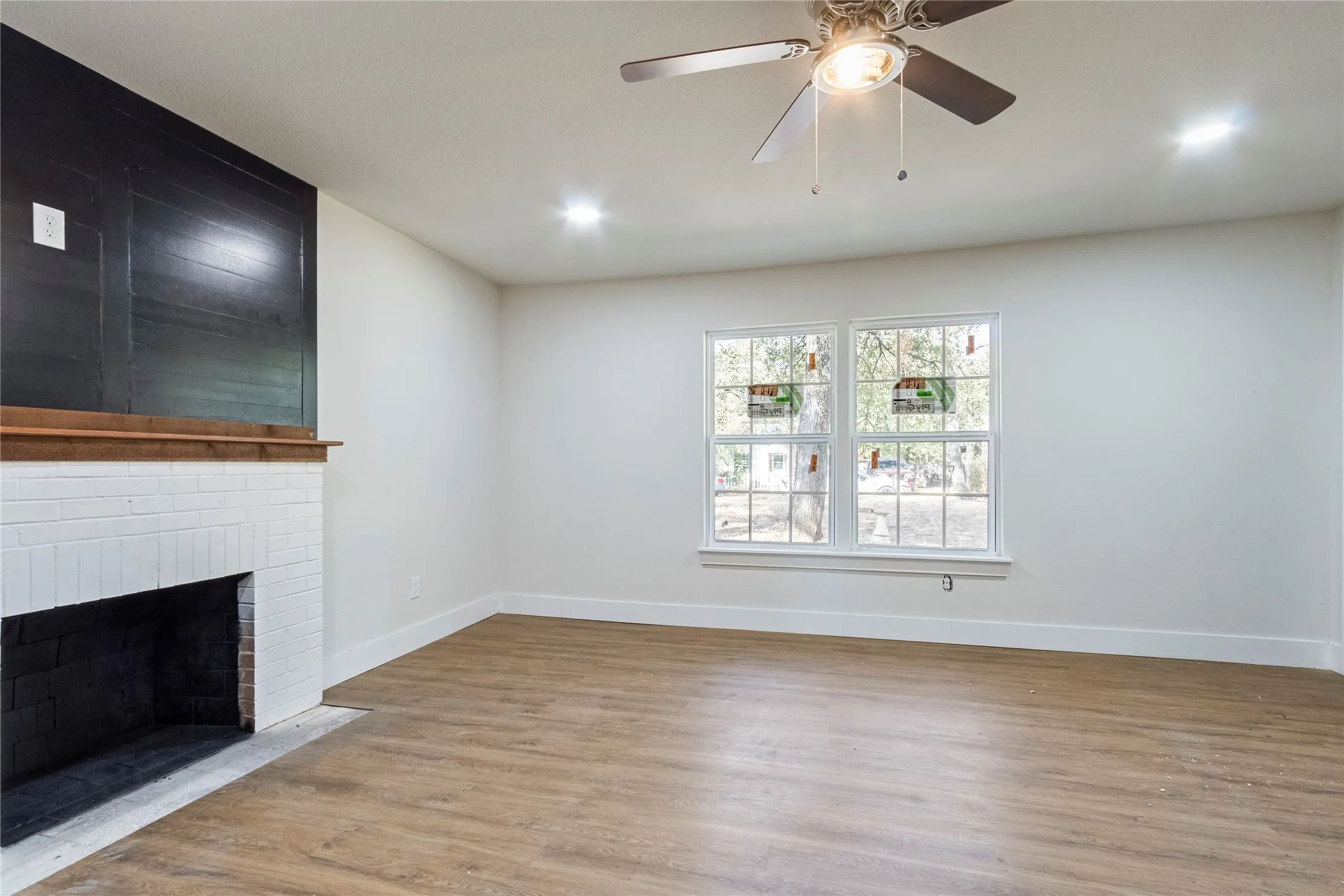 Wood-finish flooring with a white brick fireplace and a dark wood mantel