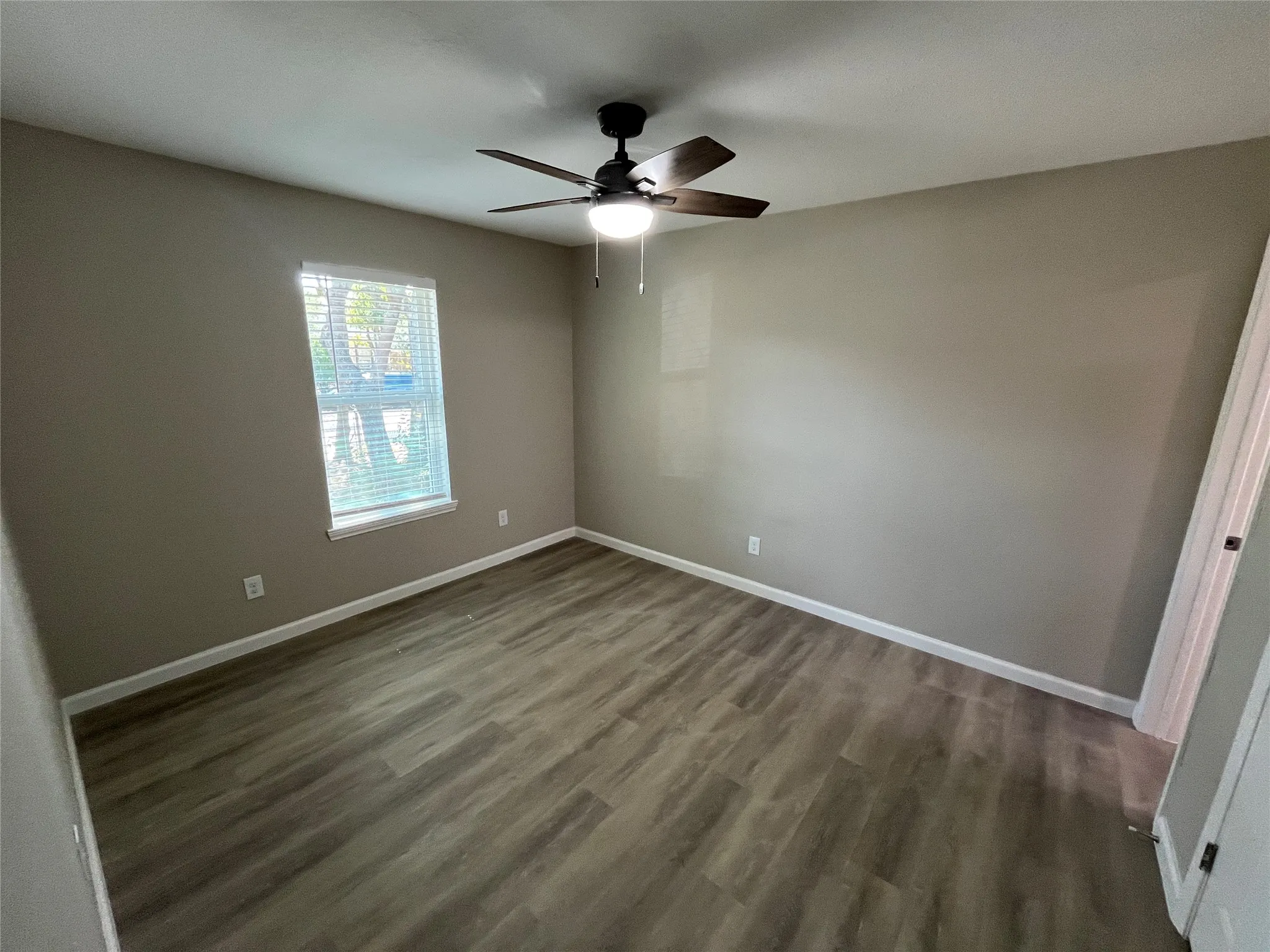 Wood-finish flooring, single window with blinds, ceiling fan with integrated lighting, and neutral wall tones