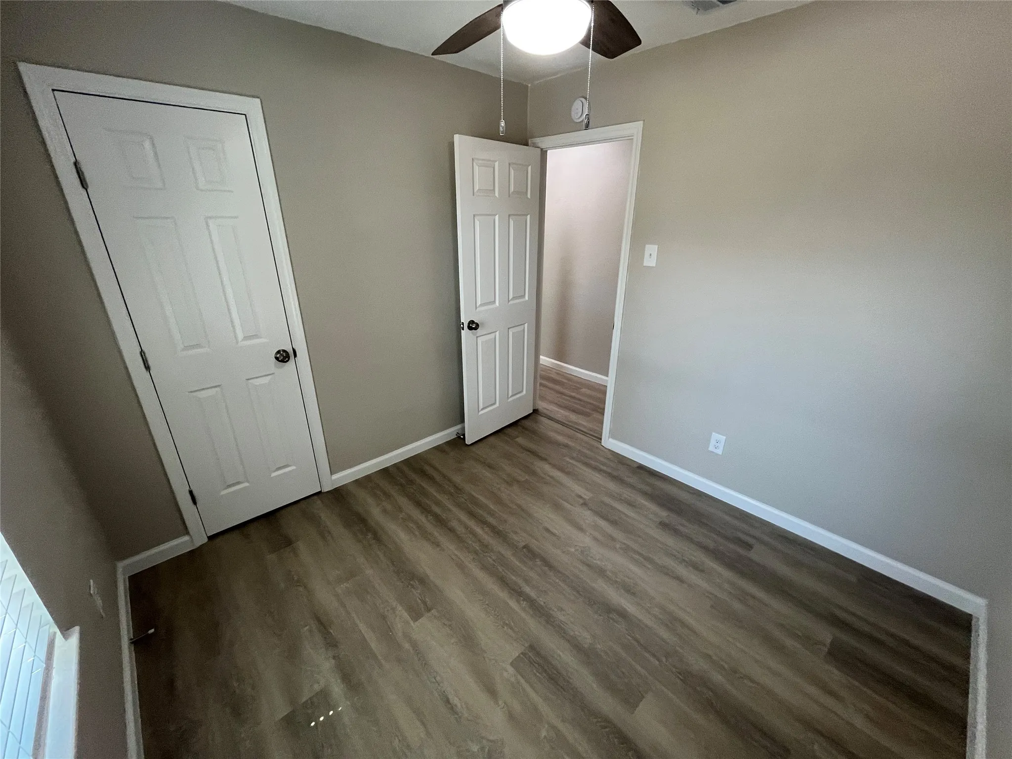 Wood-finish flooring, neutral wall color, ceiling fan with integrated lighting, and white paneled doors