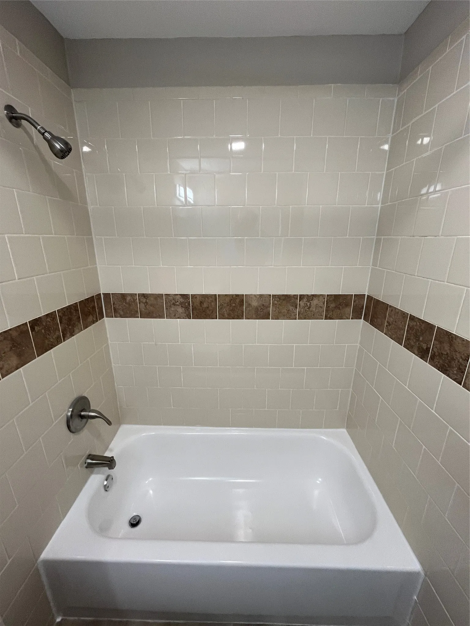 White subway tile surround with decorative accent band, white bathtub, and brushed nickel fixtures