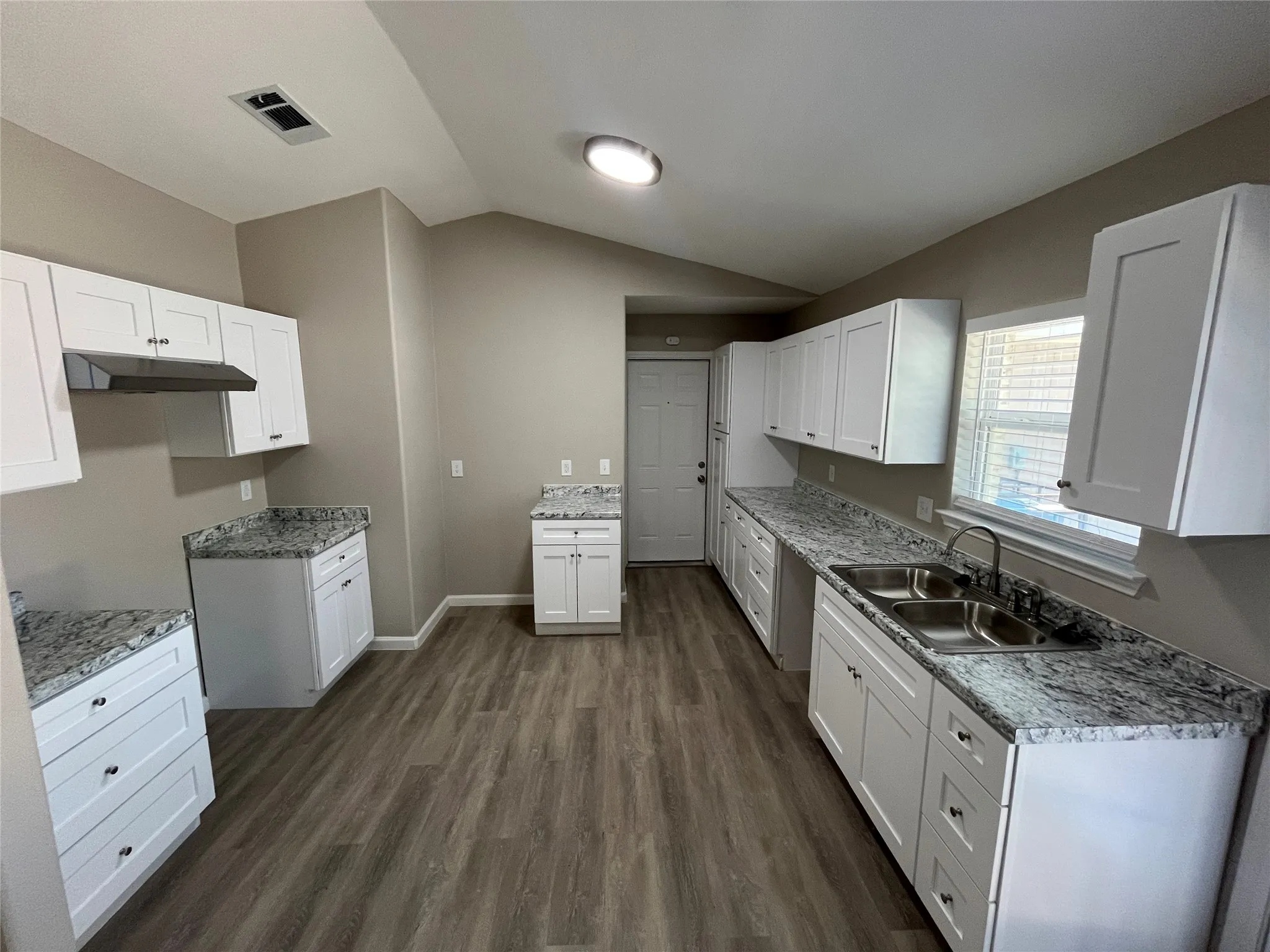 Spacious kitchen featuring white shaker cabinetry, granite-patterned countertops, wood-finish flooring, a double basin stainless steel sink, and a range hood