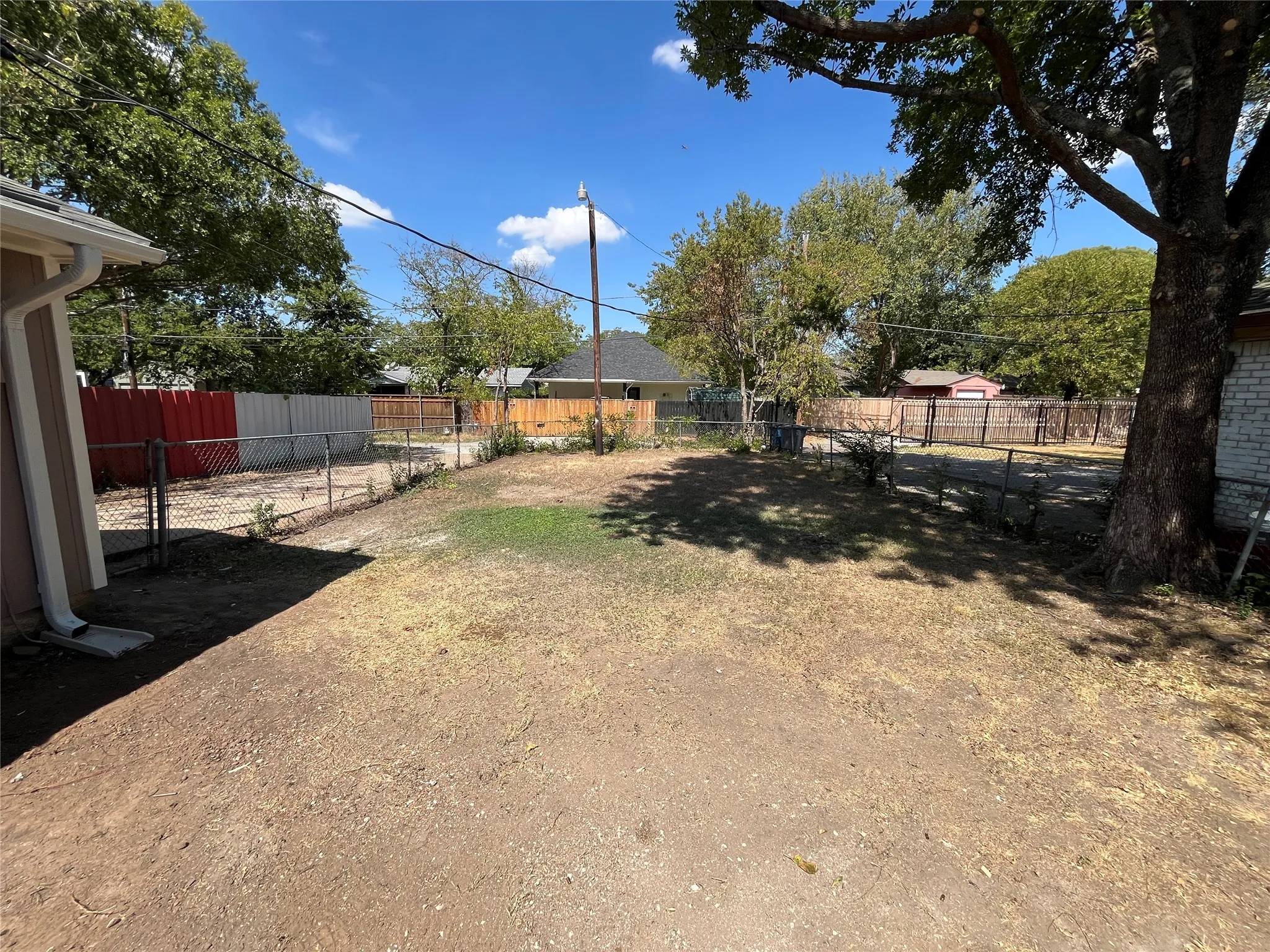 Spacious yard area enclosed by chain link fencing, featuring a mature shade tree and a portion of the property's exterior siding