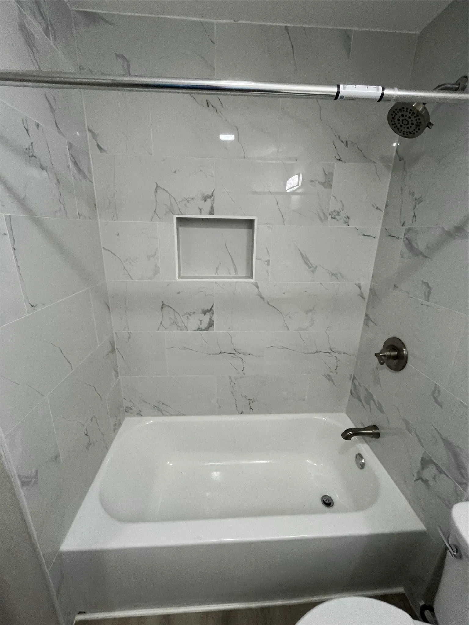 Bathtub with white subway tile surround, recessed shower niche, brushed nickel fixtures, and a chrome shower rod