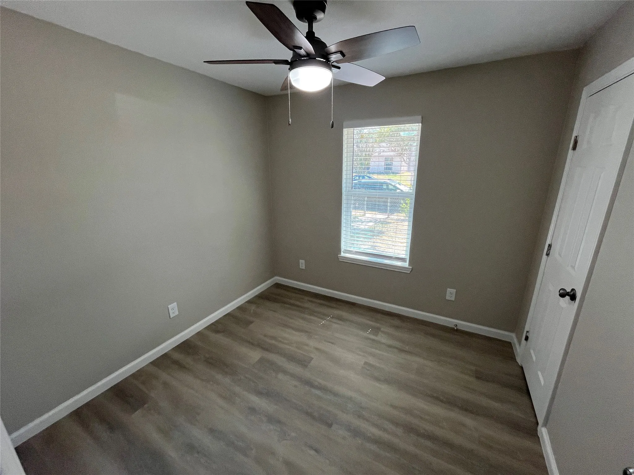 Wood-finish flooring, neutral wall tones, white trim, ceiling fan with integrated lighting, and window with blinds