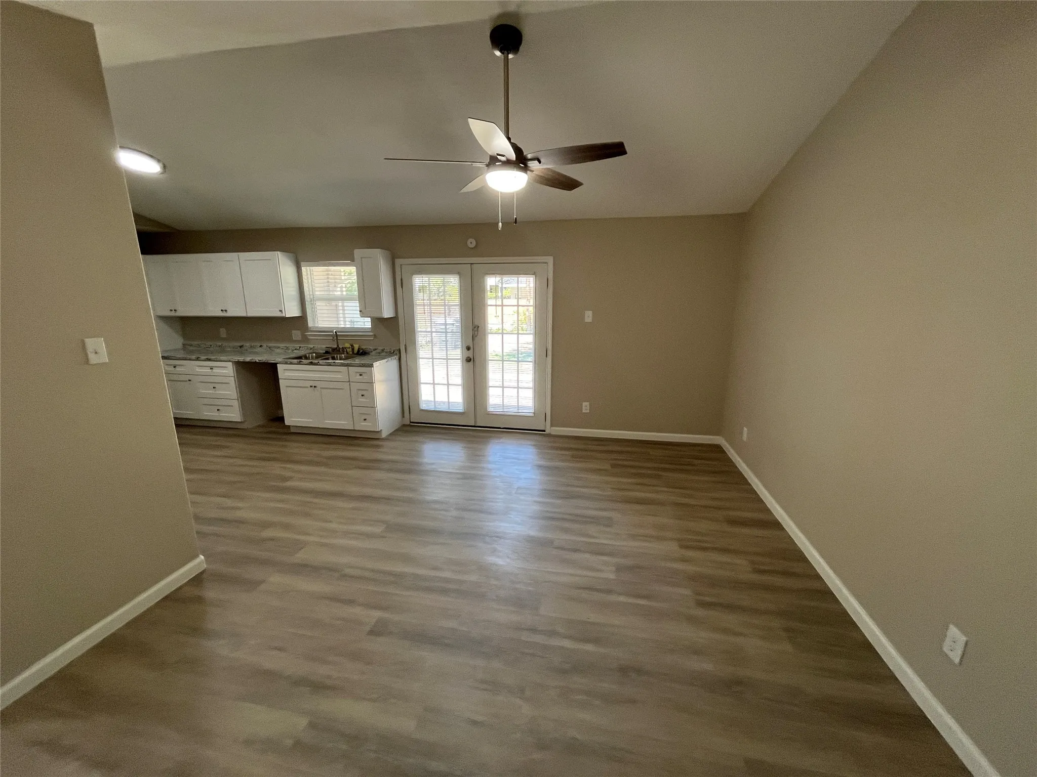 Vaulted ceiling with a ceiling fan, wood-finish flooring, white cabinetry, integrated sink, and double glass-paned doors