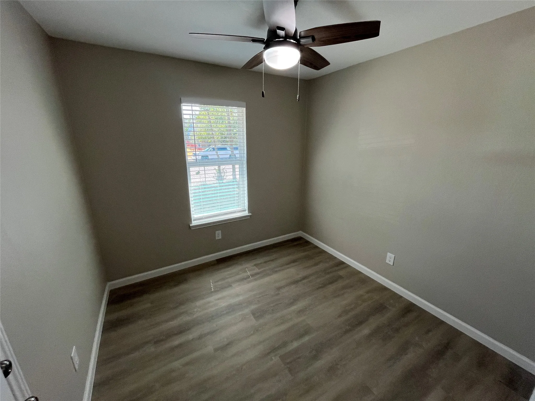 Wood-finish flooring, neutral wall tones, window with white blinds, and a ceiling fan with integrated lighting