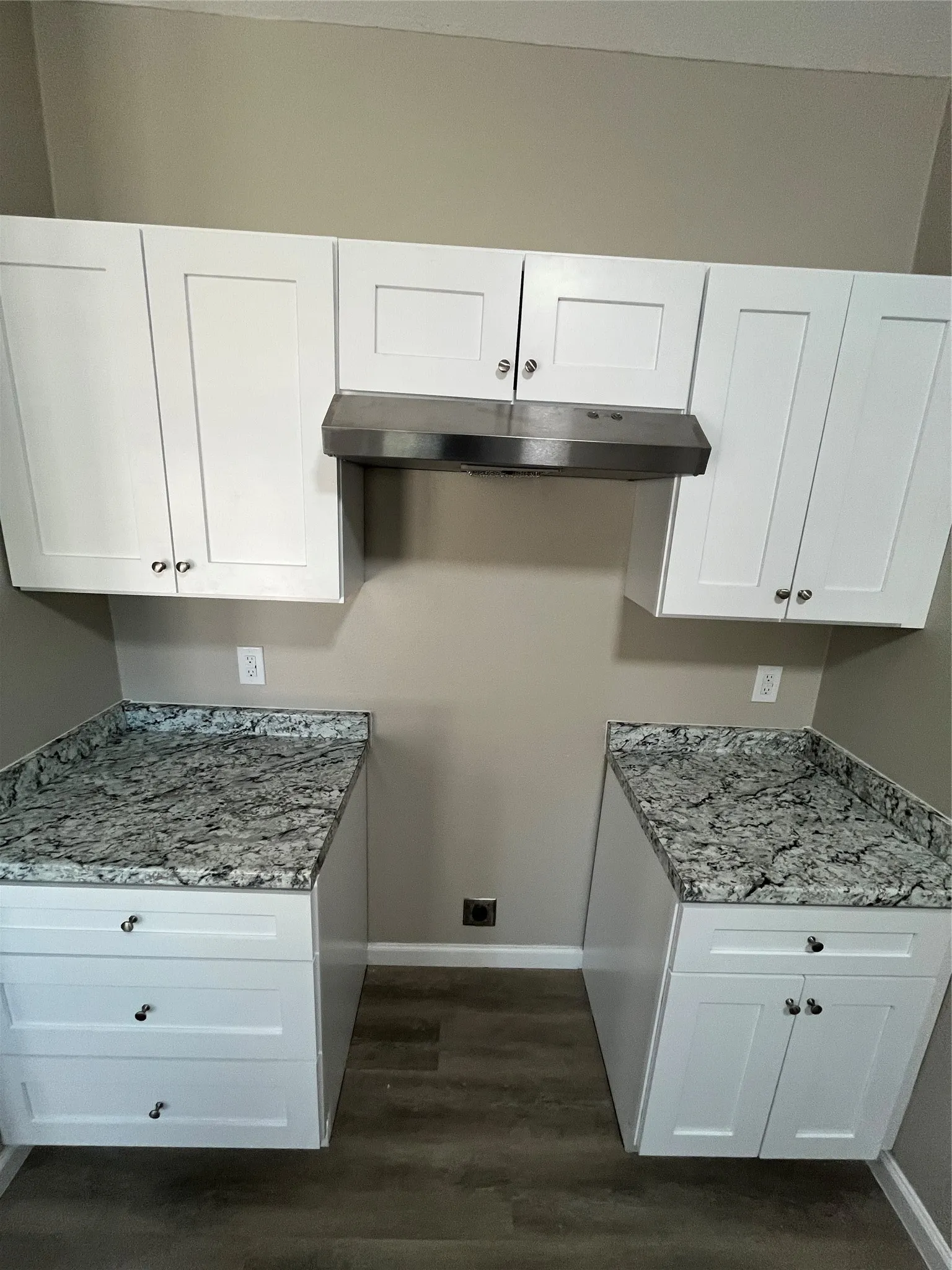 White shaker-style cabinetry, stainless steel range hood, stone-finish countertops, wood-finish flooring, and neutral wall paint