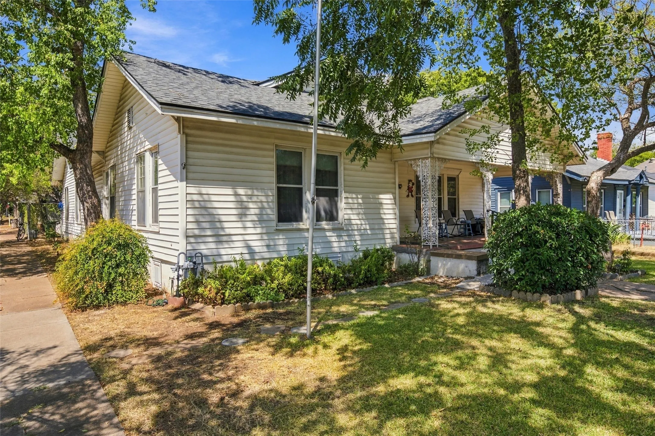 White siding exterior with a covered front porch, a gabled roof, and established landscaping