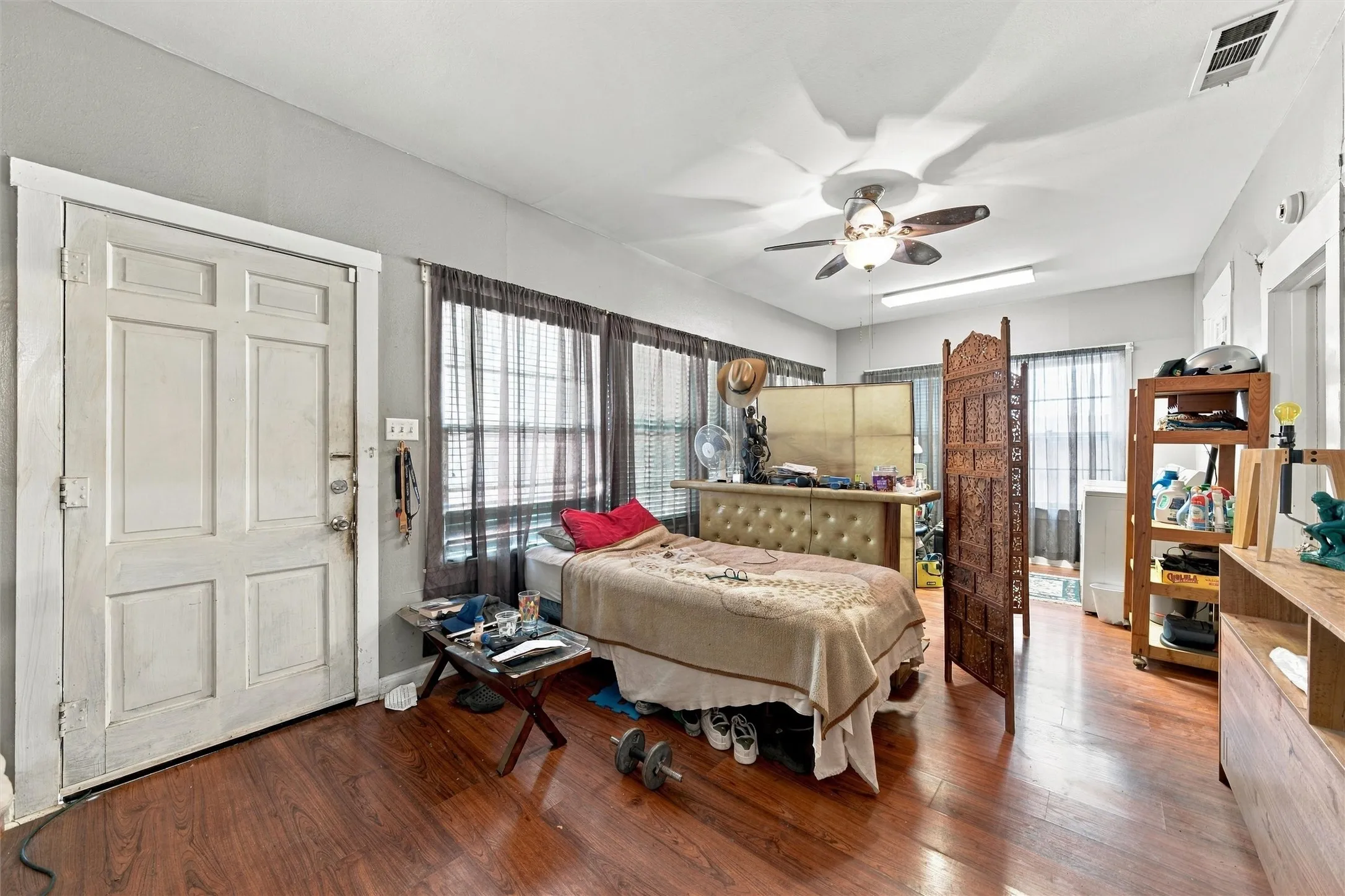 Spacious primary bedroom featuring hardwood flooring, ceiling fan with integrated lighting, French doors with sheer panel treatments, and abundant natural light from multiple windows