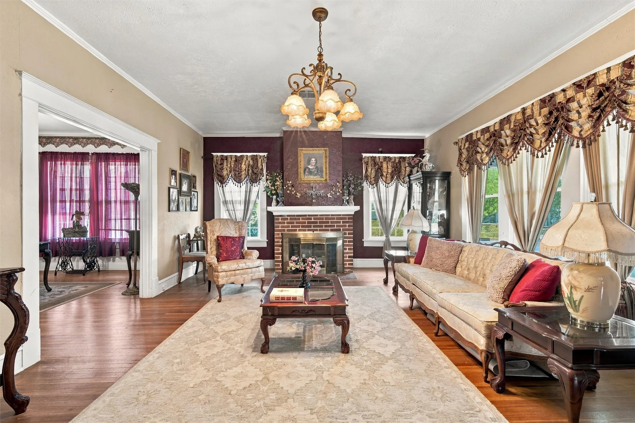 Spacious room featuring wood-finish flooring, a brick fireplace with a detailed mantel, and a multi-arm chandelier