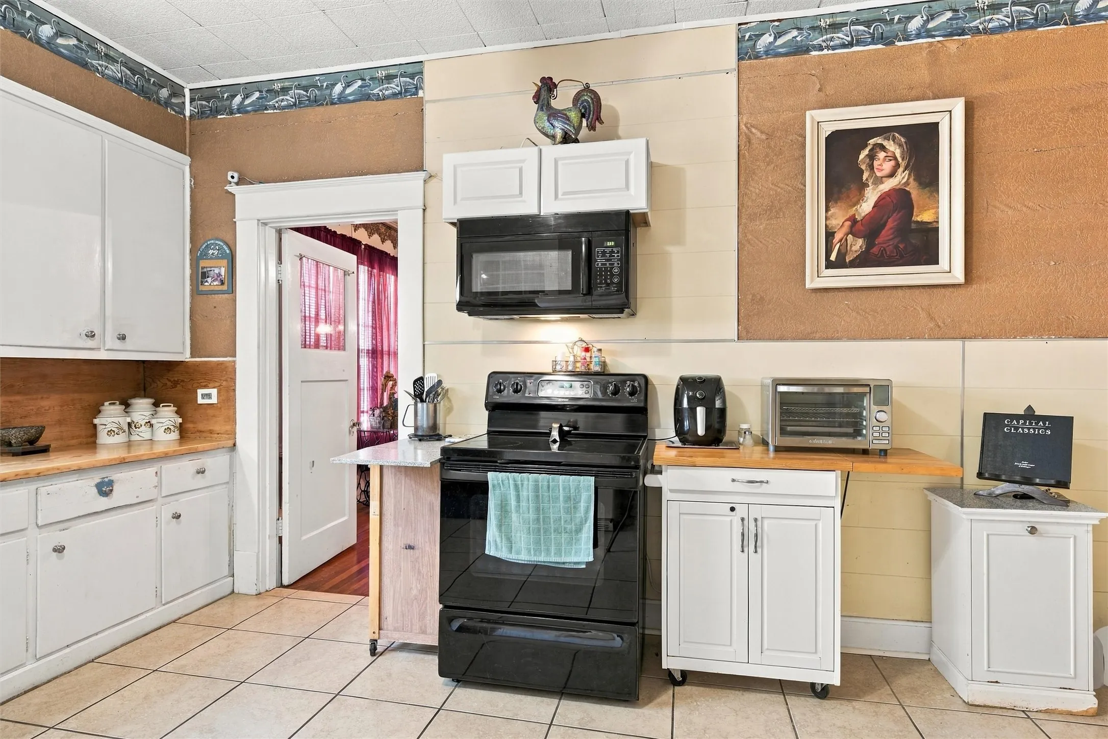 Kitchen with white cabinetry, tile flooring, a built-in microwave, a black range, and a doorway with a glass-paned door