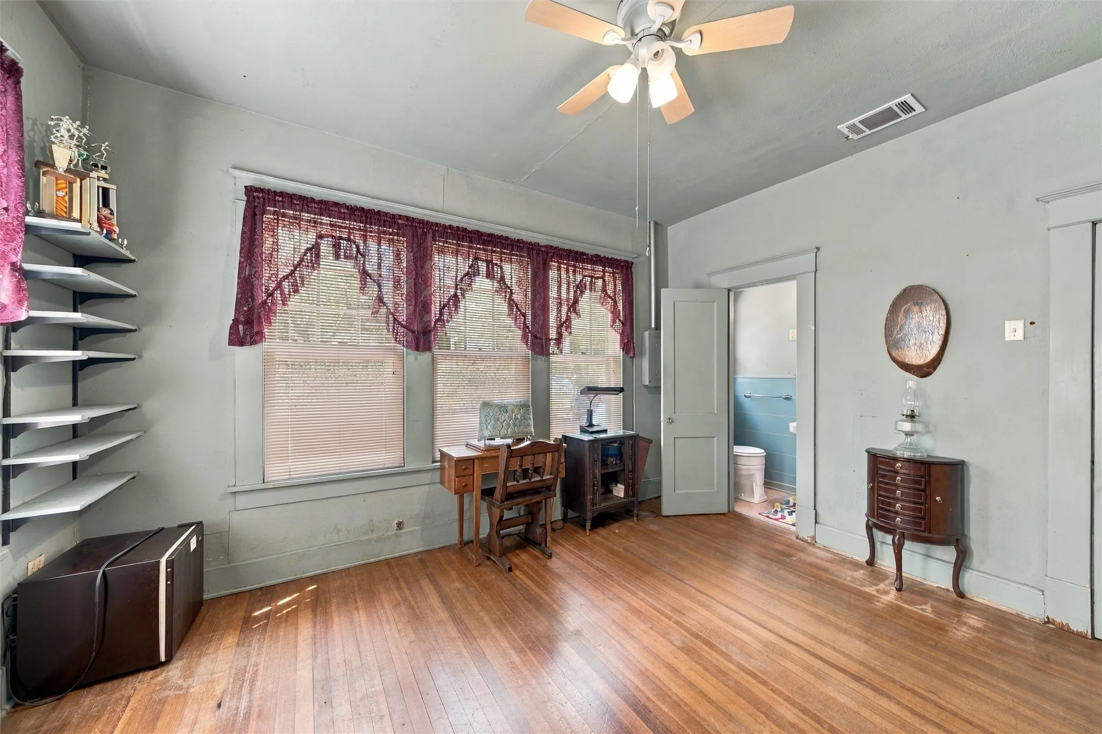 Hardwood flooring throughout, multiple windows, built-in shelving, ceiling fan, and a light-colored painted wall finish