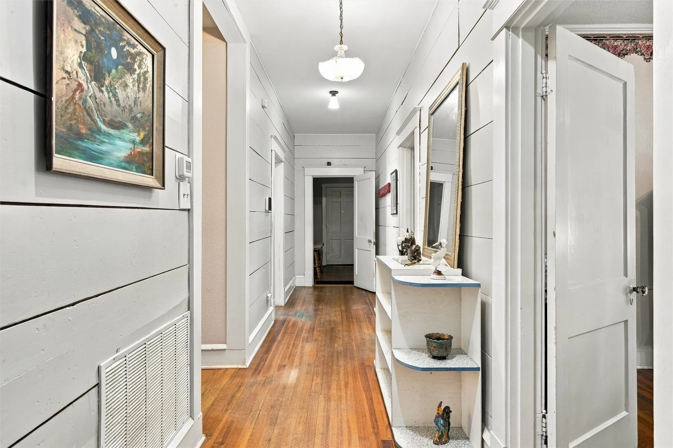 Hardwood flooring throughout, shiplap wall paneling, built-in shelving unit, interior doors, and ceiling-mounted light fixtures