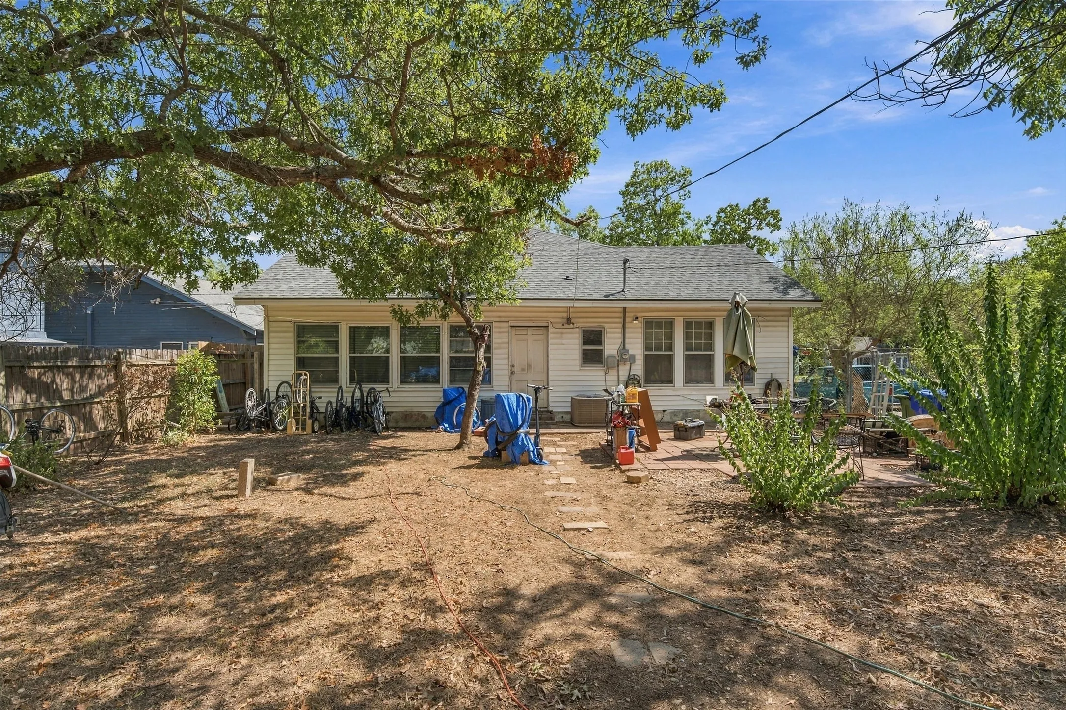 Rear exterior with white siding and multiple windows, featuring a composition shingle roof and a paved patio area