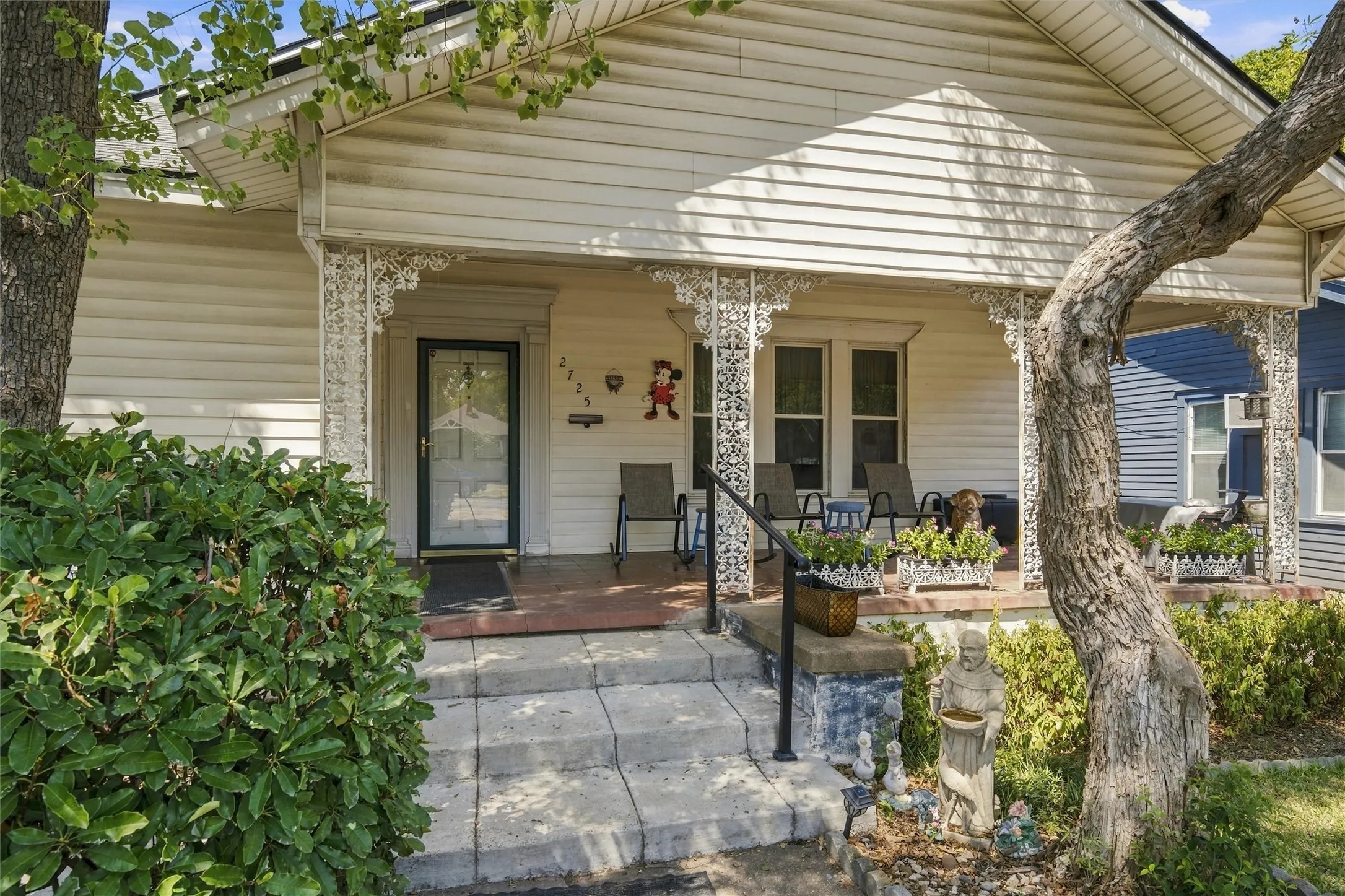 Covered front porch with decorative wrought iron support columns, concrete steps, and a black metal handrail