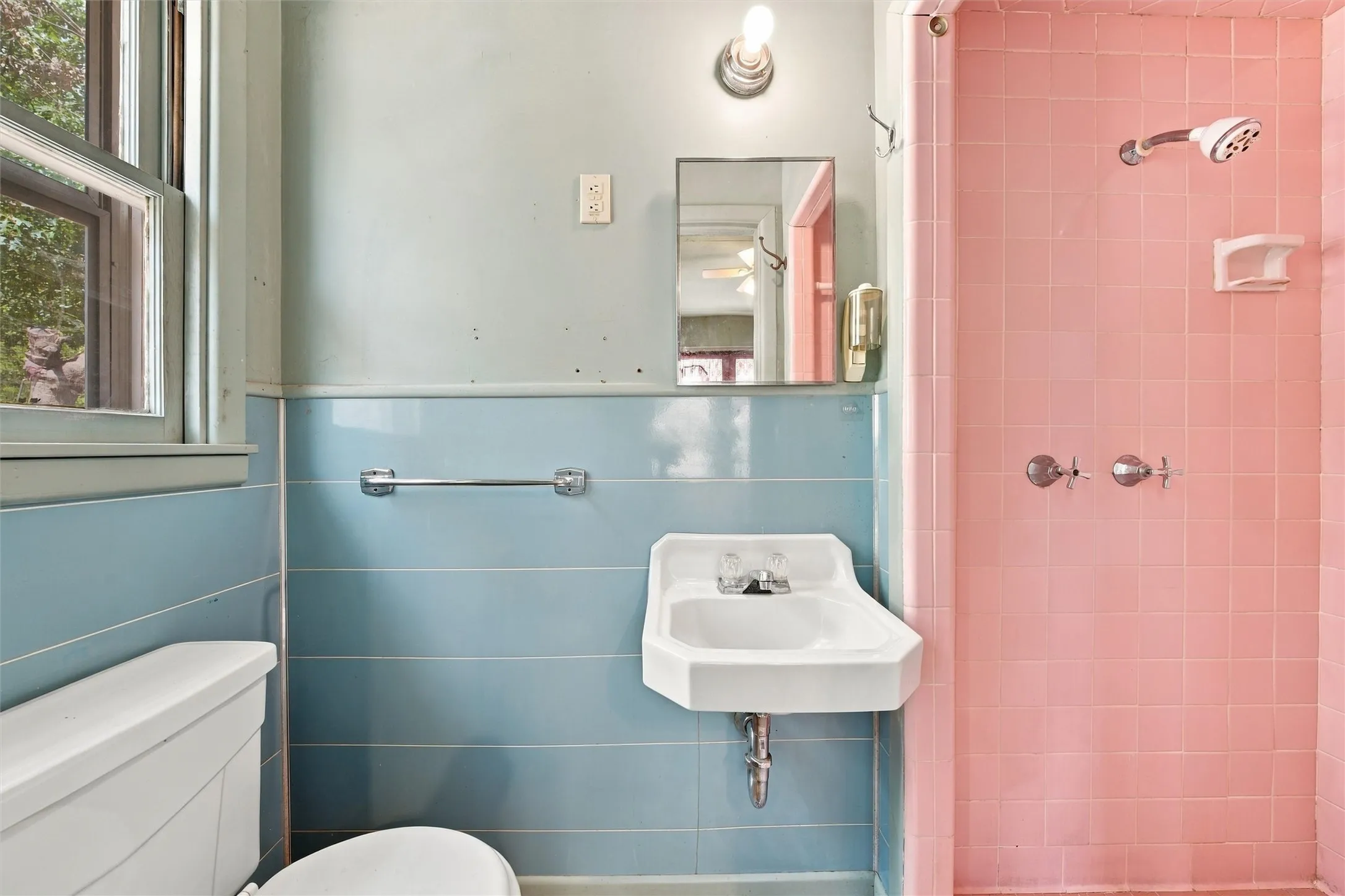 Bathroom featuring a pedestal sink, wall-mounted mirror, overhead lighting, and a shower with tile surround