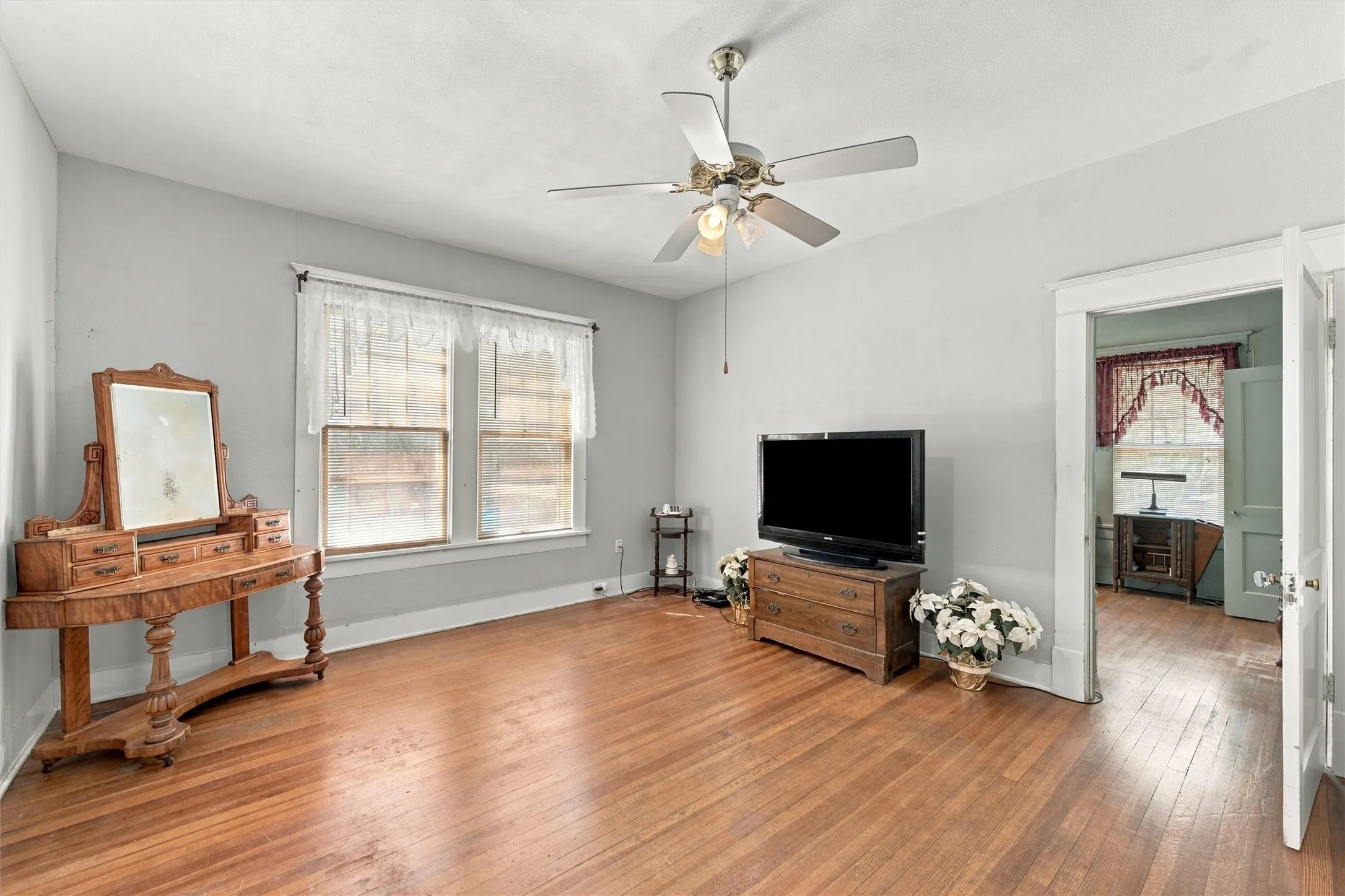 Wood-finish flooring, light gray wall paint, white trim, dual windows, and a ceiling fan with integrated lighting