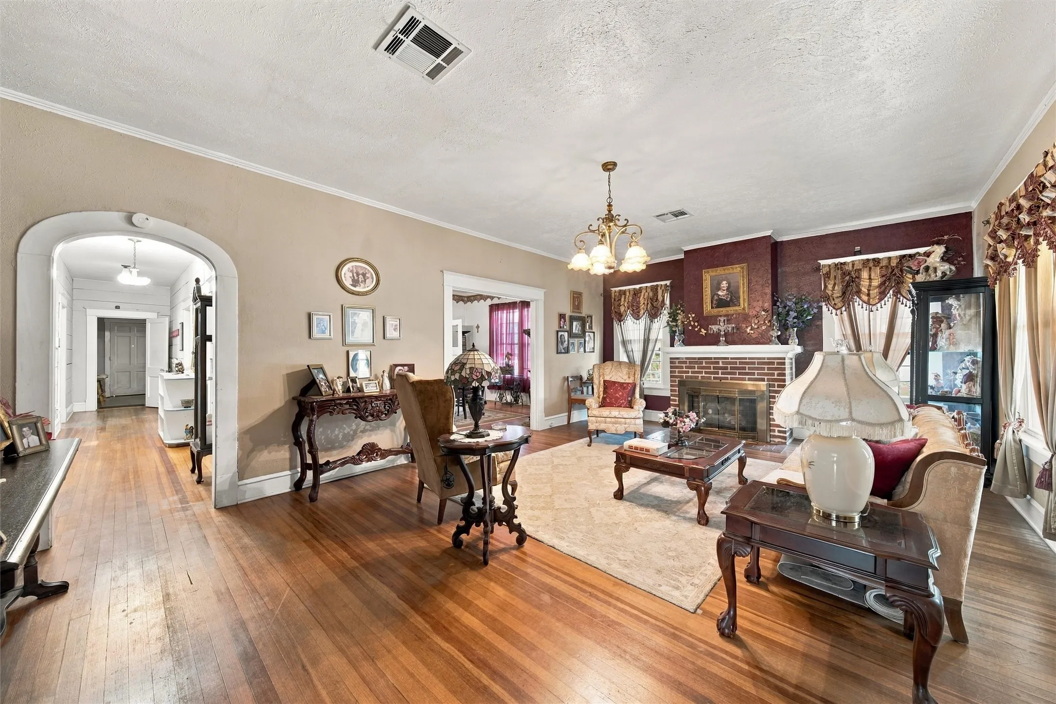 Hardwood flooring throughout, brick fireplace with mantel, arched entryway, and a chandelier