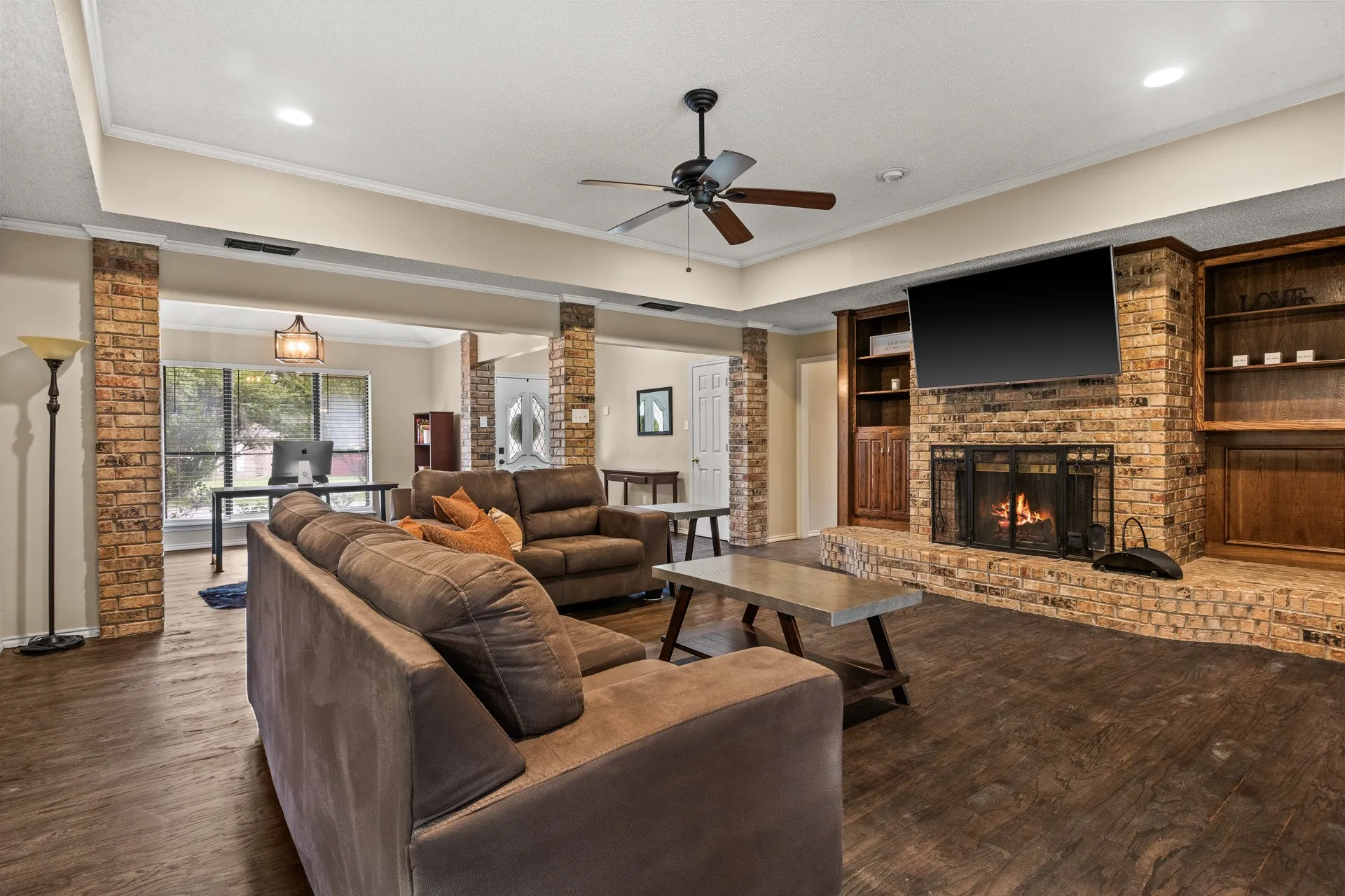 Living room featuring wood finished floors, ornate columns, ceiling fan, a fireplace, and ornamental molding