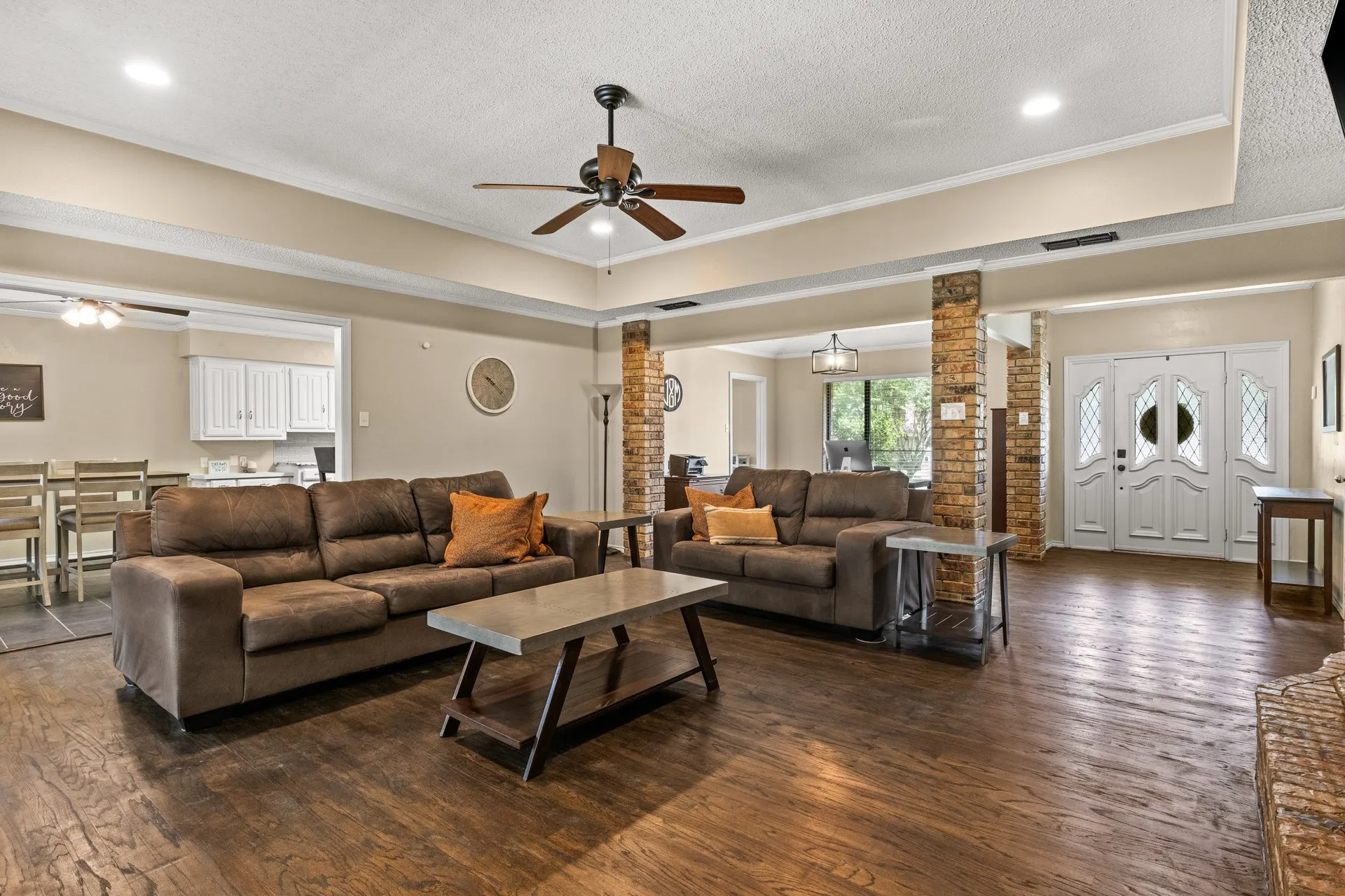 Living room featuring ornate columns, ceiling fan, dark wood-type flooring, a textured ceiling, and crown molding