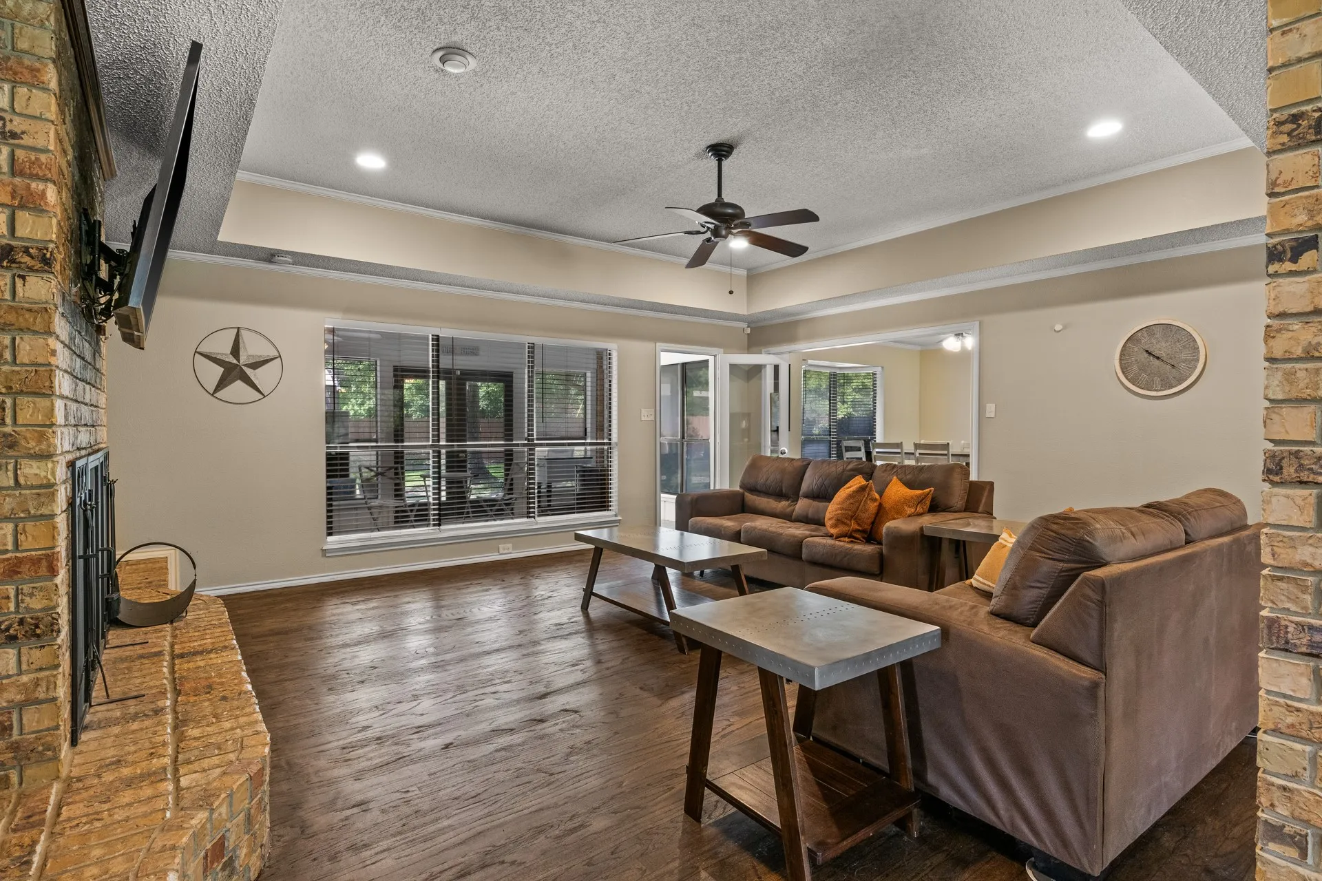Living room with a textured ceiling, ceiling fan, wood finished floors, a brick fireplace, and recessed lighting