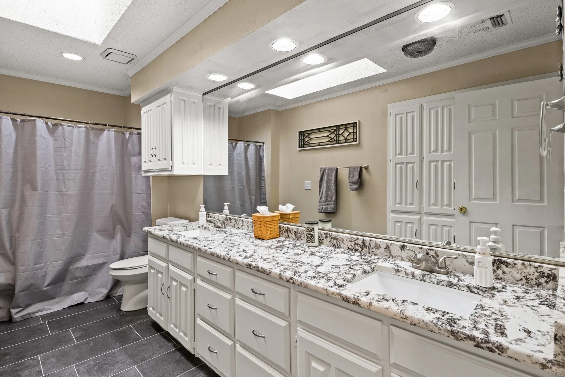 Full bath with a skylight, recessed lighting, double vanity, ornamental molding, and tile patterned floors