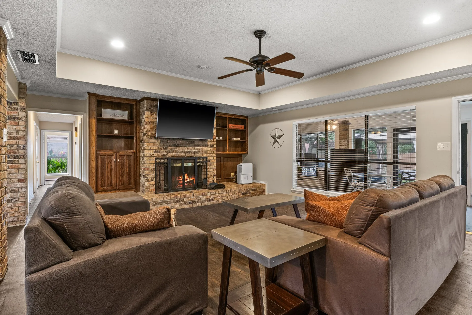 Living room with a brick fireplace, a ceiling fan, crown molding, a textured ceiling, and a tray ceiling