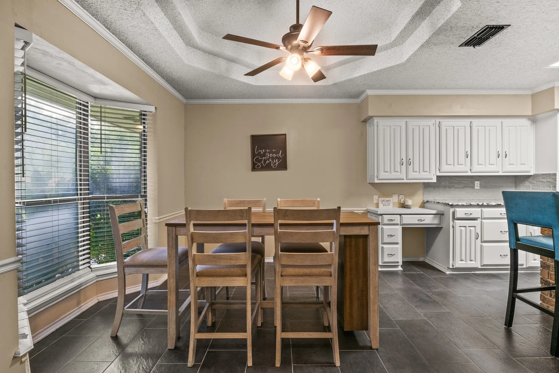 Dining space featuring ceiling fan, a textured ceiling, crown molding, dark tile patterned flooring, and a tray ceiling