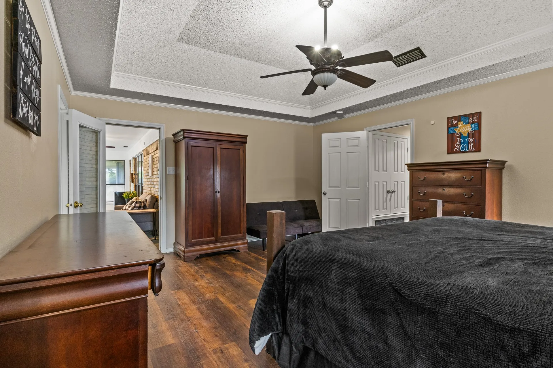 Bedroom with a raised ceiling, dark wood-style flooring, crown molding, a textured ceiling, and a ceiling fan