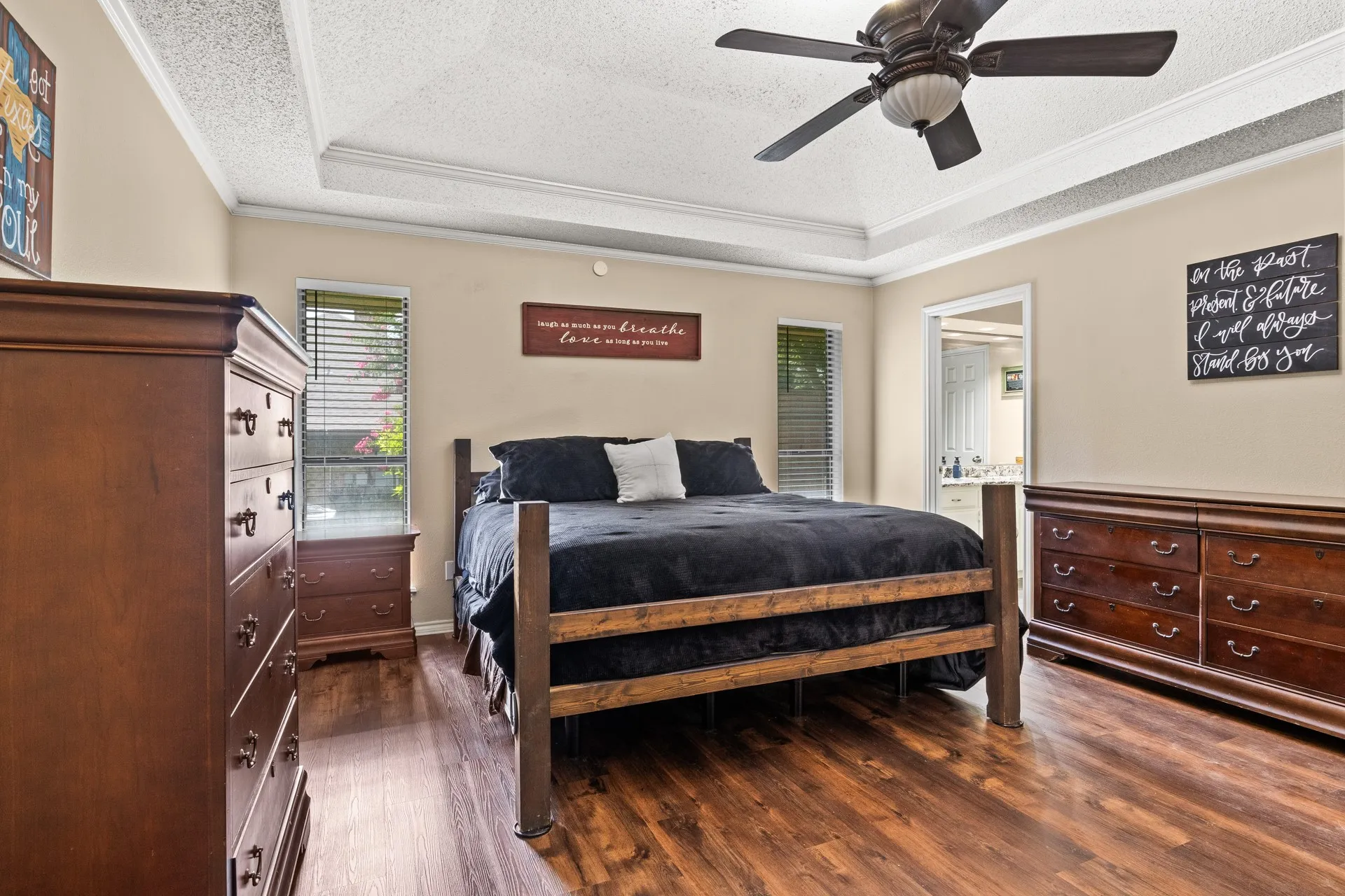 Bedroom with a textured ceiling, crown molding, a raised ceiling, wood finished floors, and a ceiling fan