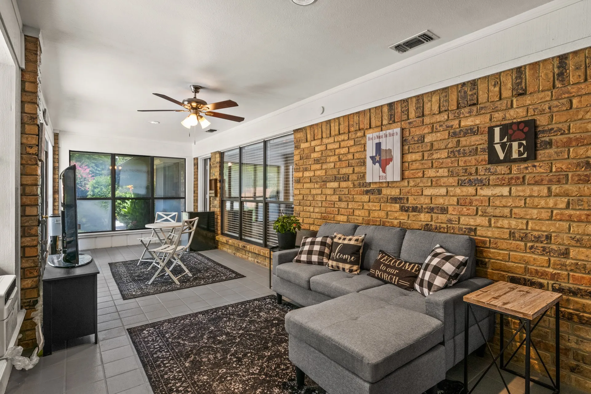 Living area with tile patterned flooring, ceiling fan, and brick wall