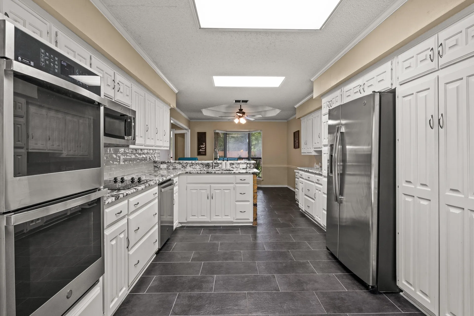 Kitchen with appliances with stainless steel finishes, a peninsula, white cabinets, a textured ceiling, and ornamental molding