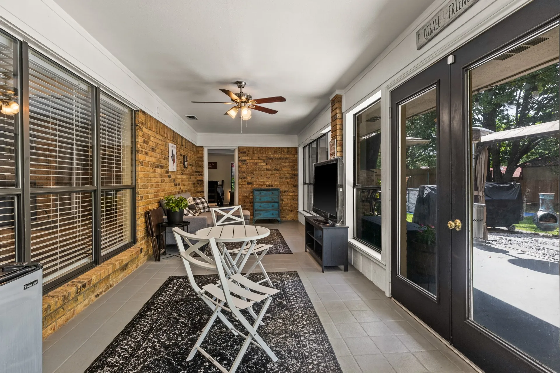 Sunroom / solarium with tile patterned flooring, a ceiling fan, and brick wall