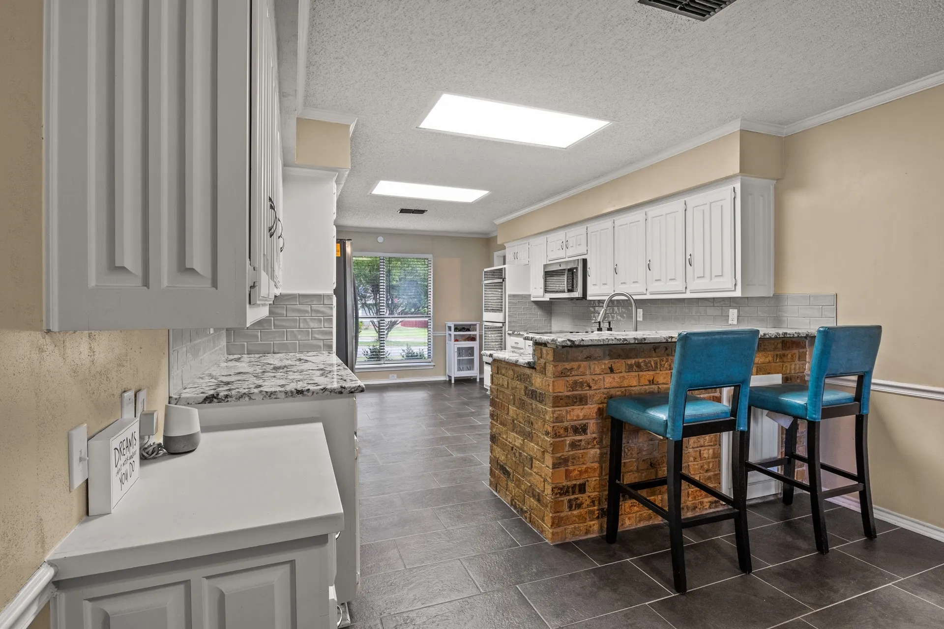 Kitchen featuring stainless steel microwave, decorative backsplash, a peninsula, a textured ceiling, and a breakfast bar