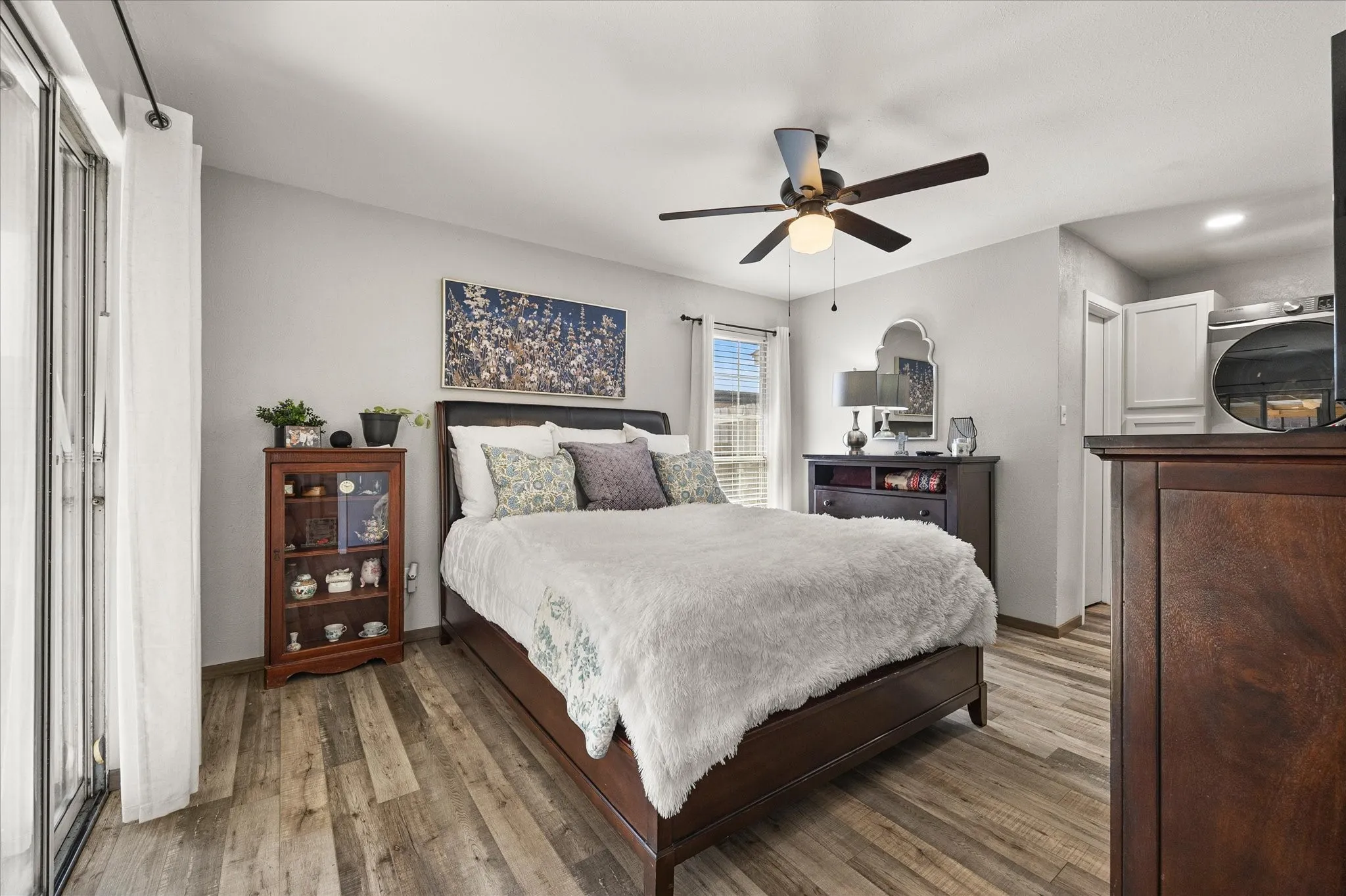 Wood-finish vinyl plank flooring, ceiling fan with integrated lighting, white walls, and sliding glass door