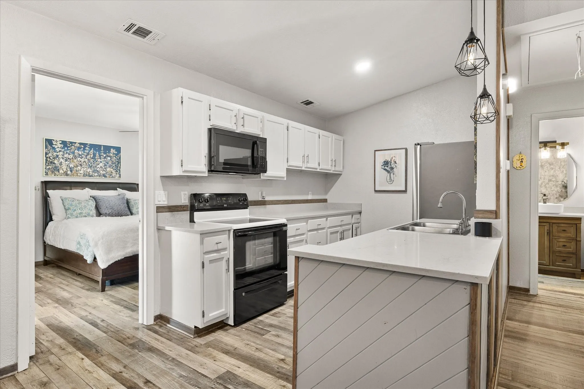 Kitchen featuring white cabinetry, stainless steel sink, wood-finish vinyl plank flooring, and pendant lighting