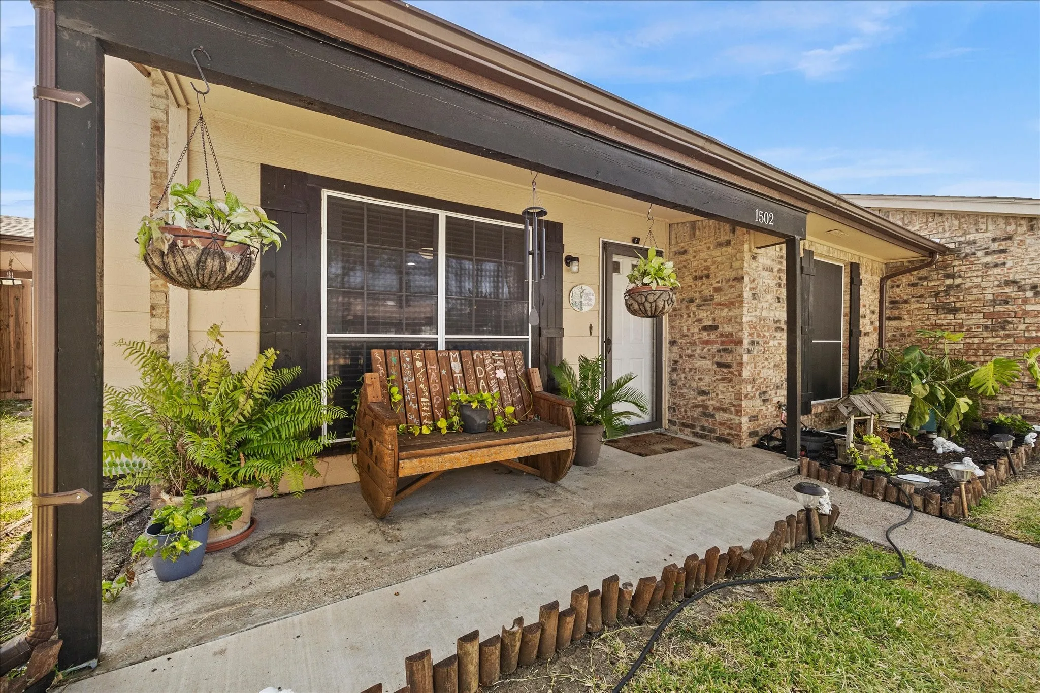 Brick facade, covered entry, front porch, concrete pathway, and landscaping with decorative wood edging
