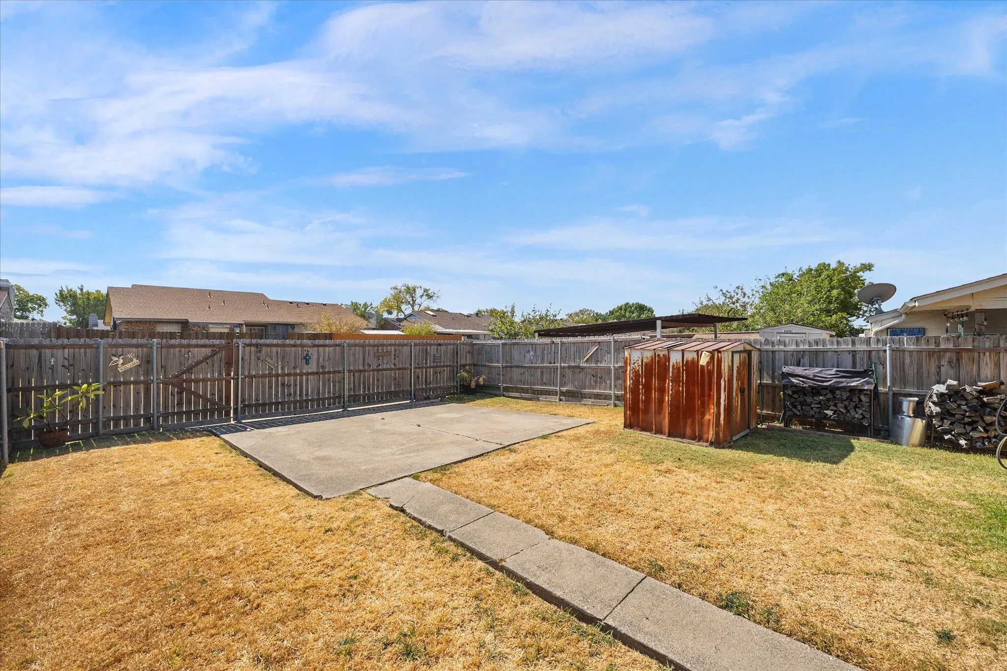 Expansive backyard concrete driveway featuring a concrete patio, wood fencing, and a concrete pathway