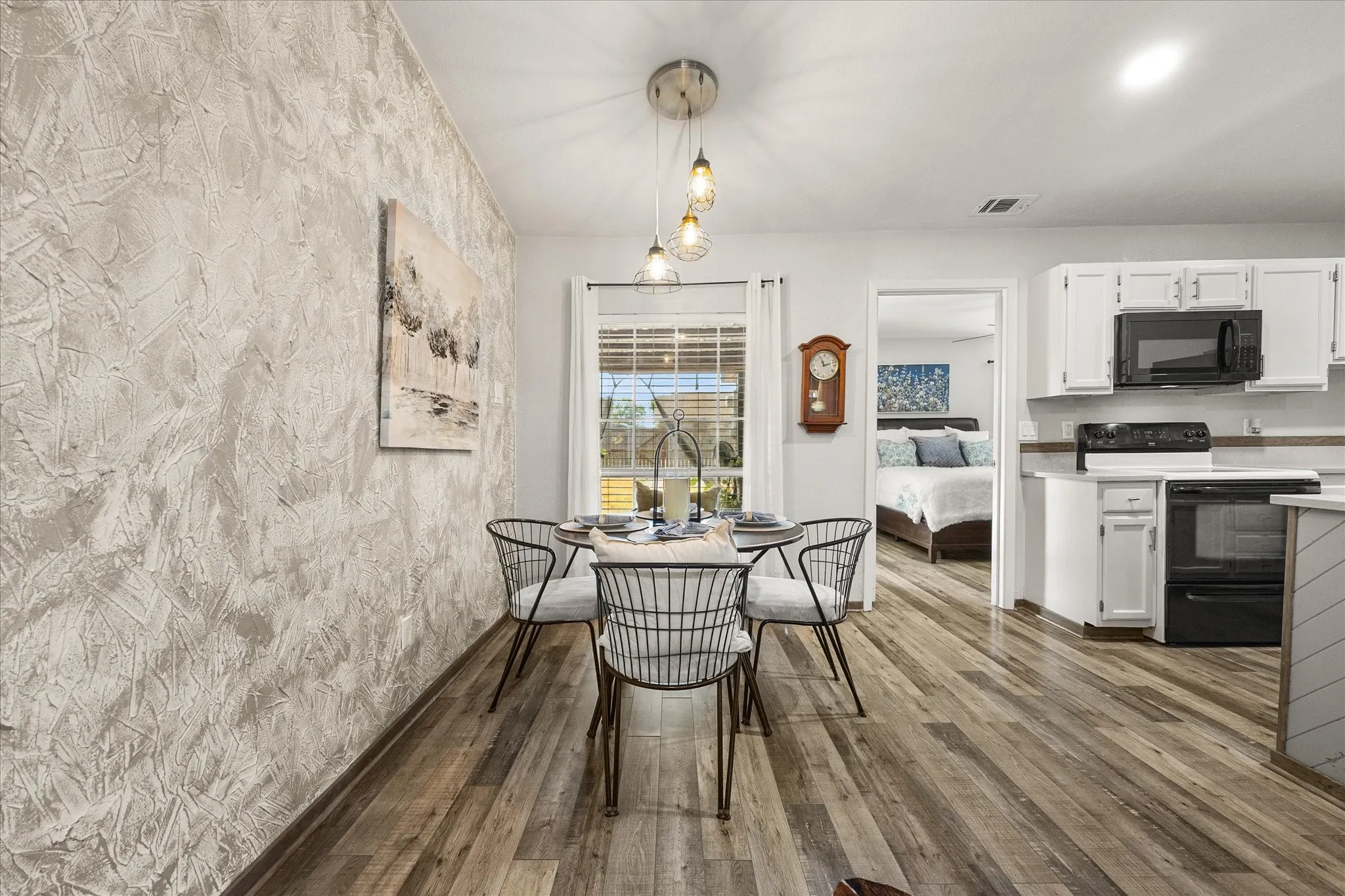 Textured accent wall, recessed lighting, white cabinetry, and black and white appliances