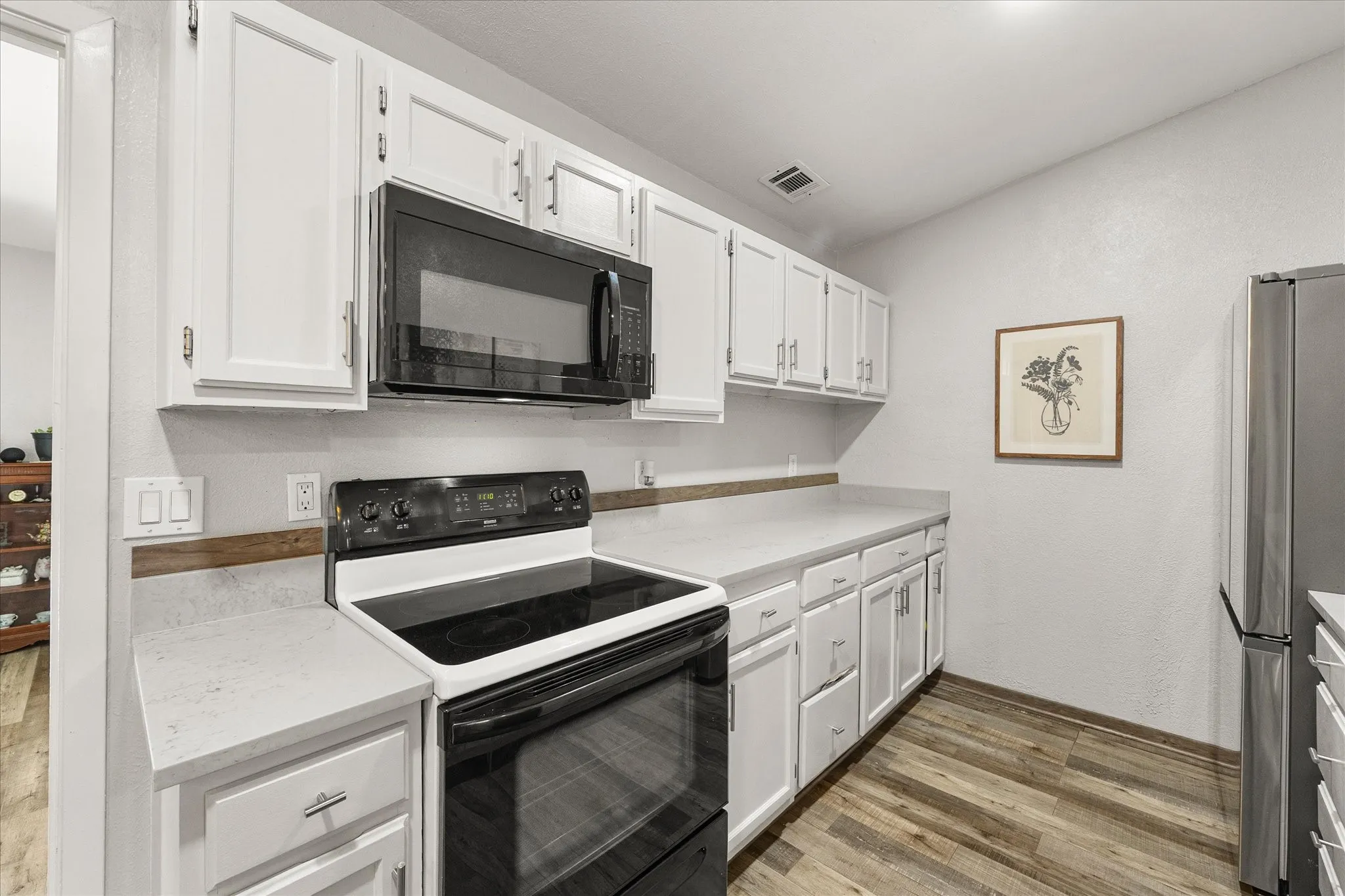 White cabinetry with silver-tone hardware, dark finish oven top and built in microwave, light-toned countertops