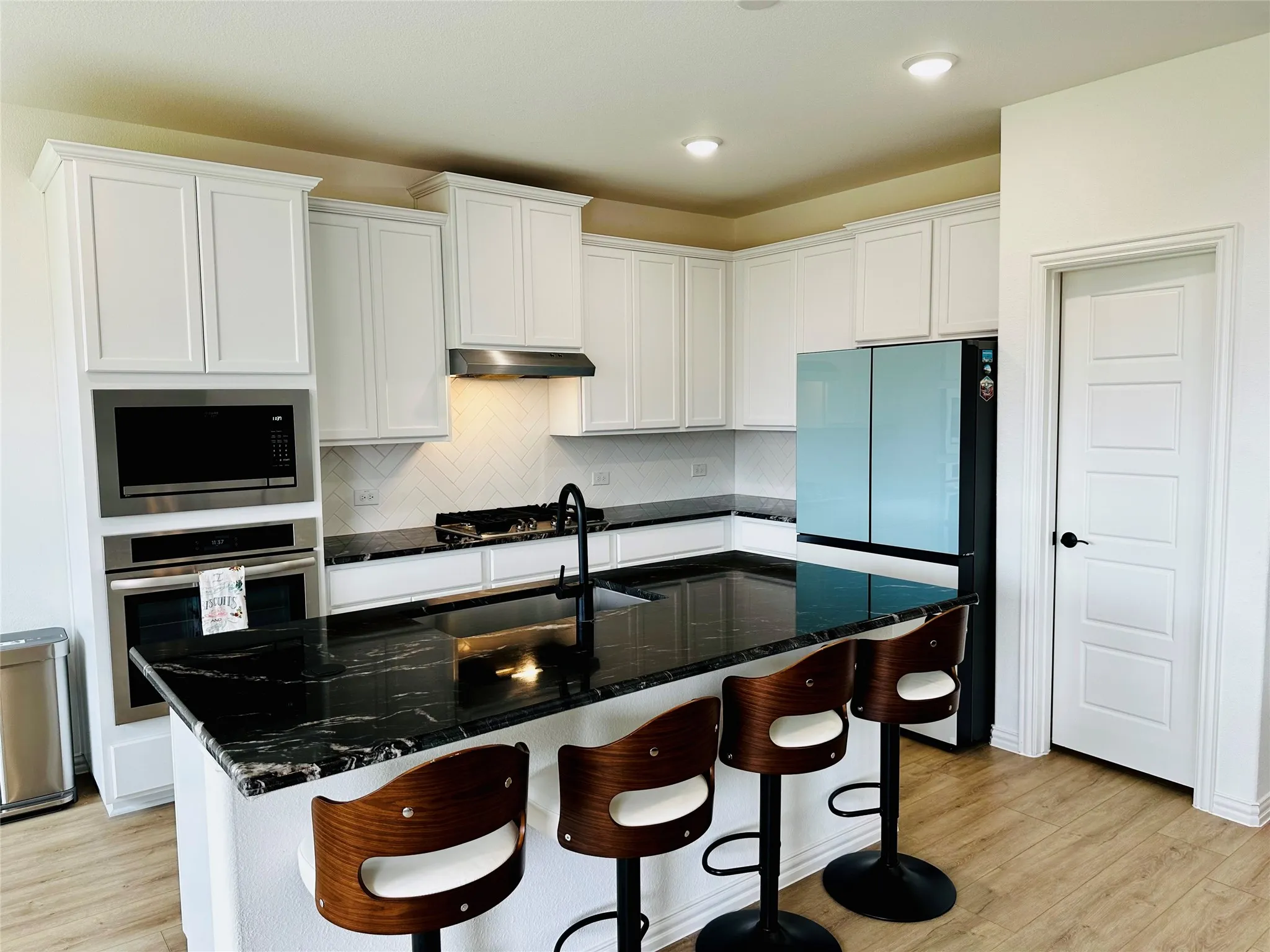 Kitchen featuring white cabinetry, black stone countertops, a subway tile backsplash, stainless steel appliances, and wood-finish flooring
