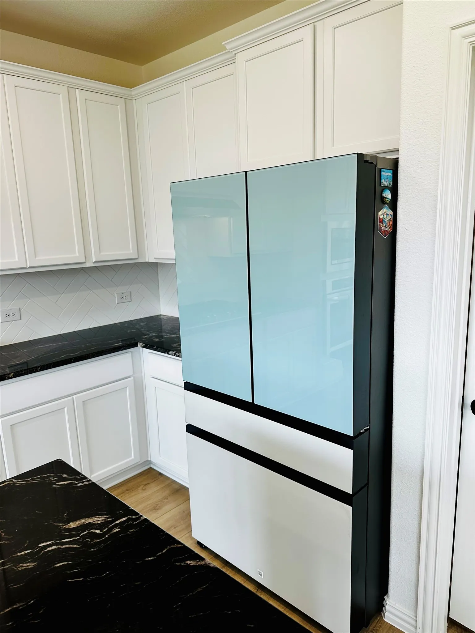 White shaker-style cabinetry with crown molding, dark stone countertops, wood-finish flooring, and a white subway tile backsplash