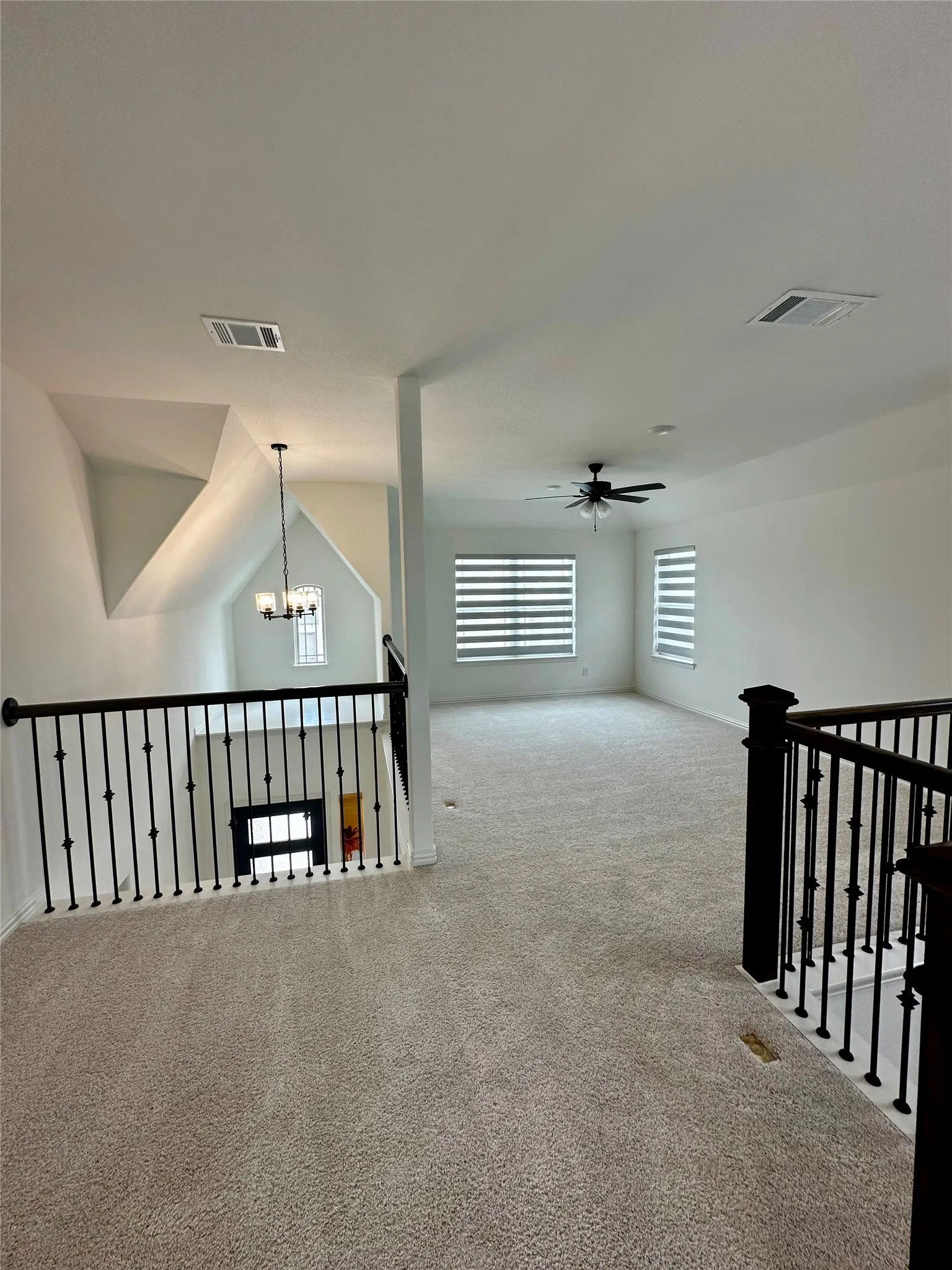 Carpeted loft area with wrought iron railings, an overhead ceiling fan, and multiple windows with horizontal blinds