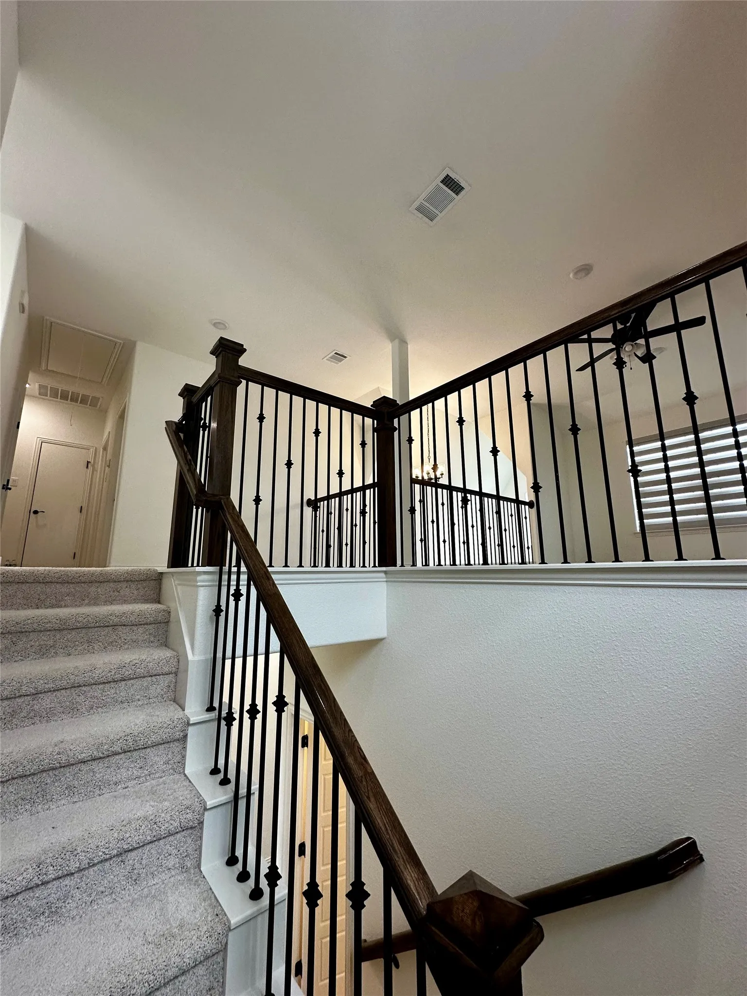 Carpeted staircase with dark wood handrail and decorative iron balusters, leading to an open landing
