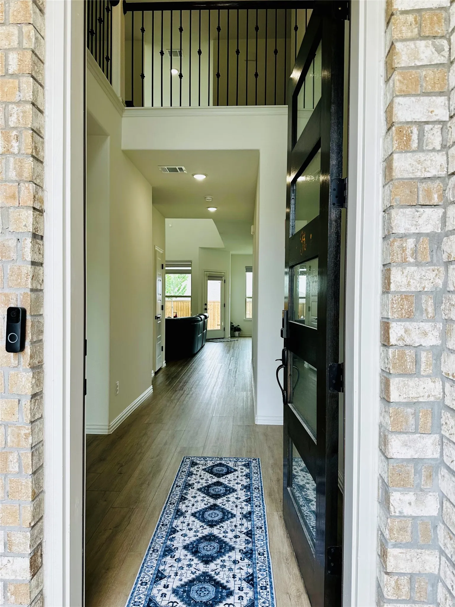 Brick exterior with an entryway featuring a contemporary glass-paneled door, wood-finish flooring, recessed lighting, and an open second-story railing
