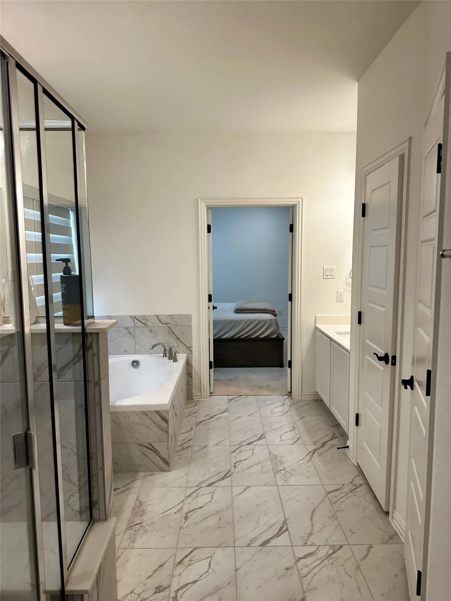 Large format tile flooring, tiled soaking tub surround, frameless glass shower enclosure, double vanity with white cabinetry, and brushed nickel fixtures