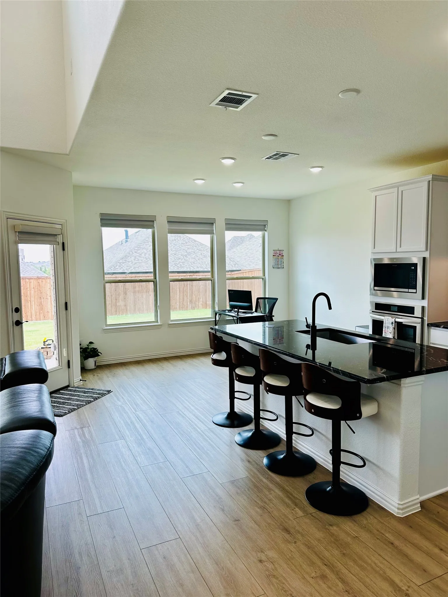 Open-concept living space with wood-finish flooring, a kitchen island featuring a dark countertop, white cabinetry with built-in appliances, and recessed ceiling lighting
