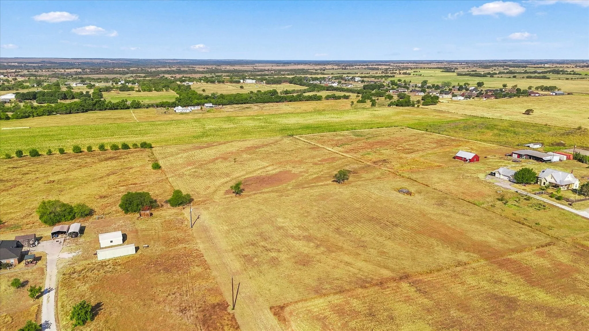 Expansive rural landscape featuring distant structures and scattered trees